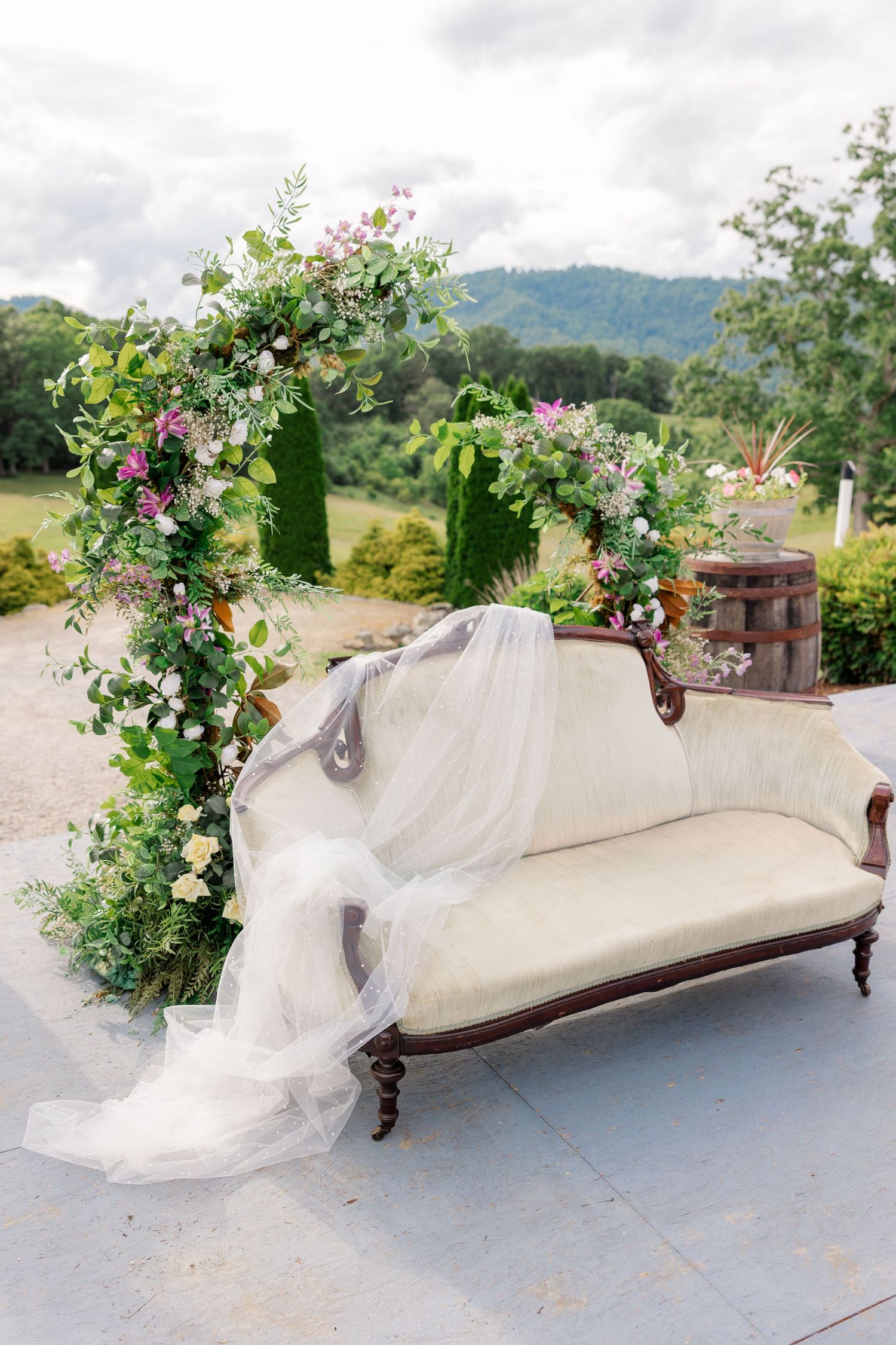 Vintage white chaise lounge decorated with floral arrangements and flowing fabric for wedding decor.