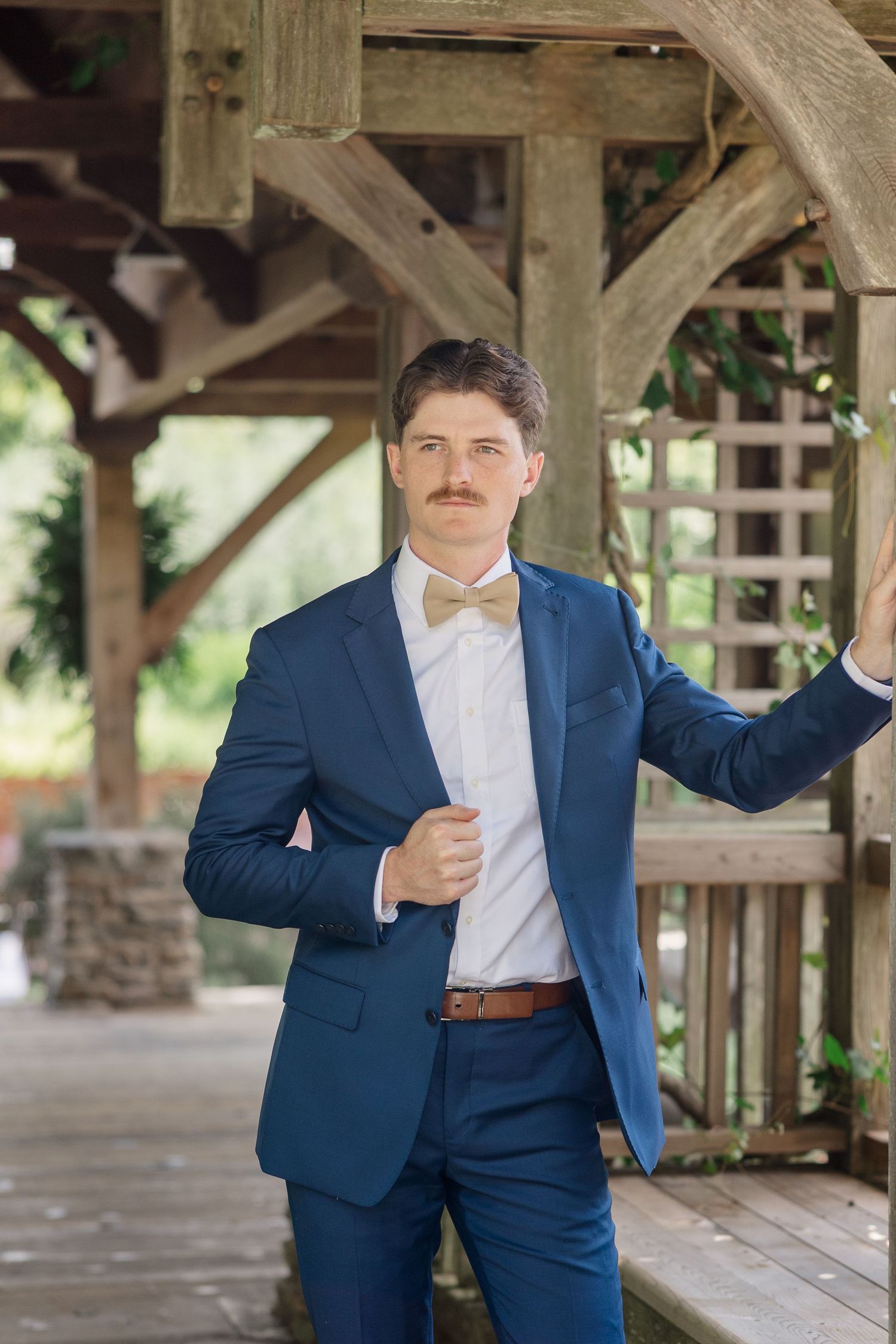 A groom in a navy blue suit and white shirt poses playfully in a covered outdoor area.