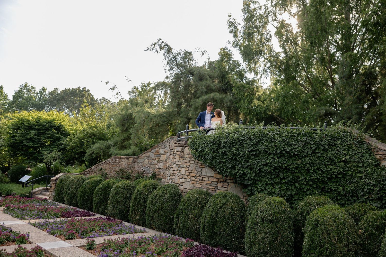 A garden wedding venue featuring manicured hedges and a decorative stone wall pathway.