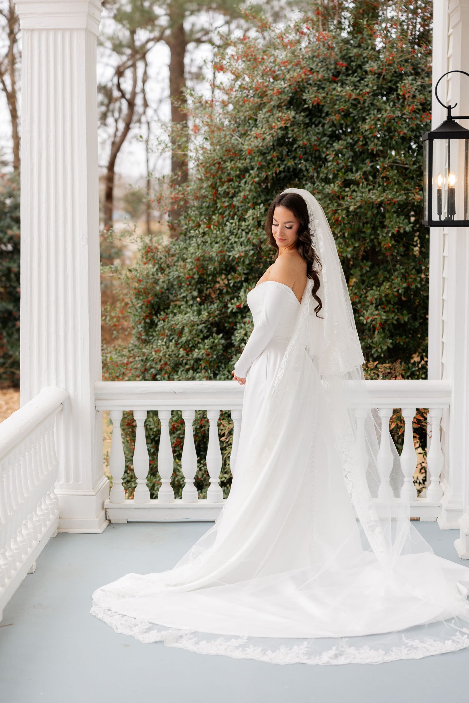 Elegant bridal portraits on a white columned porch with flowing dress and veil against green foliage.