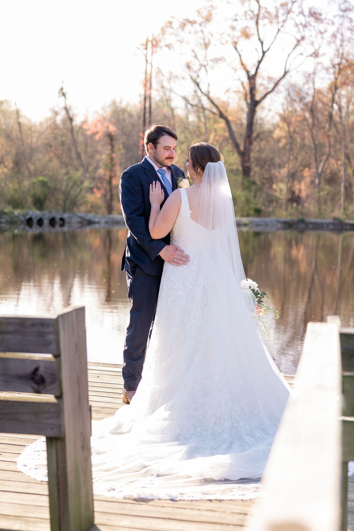 Newlyweds sharing a romantic moment on a wooden dock by a lake.