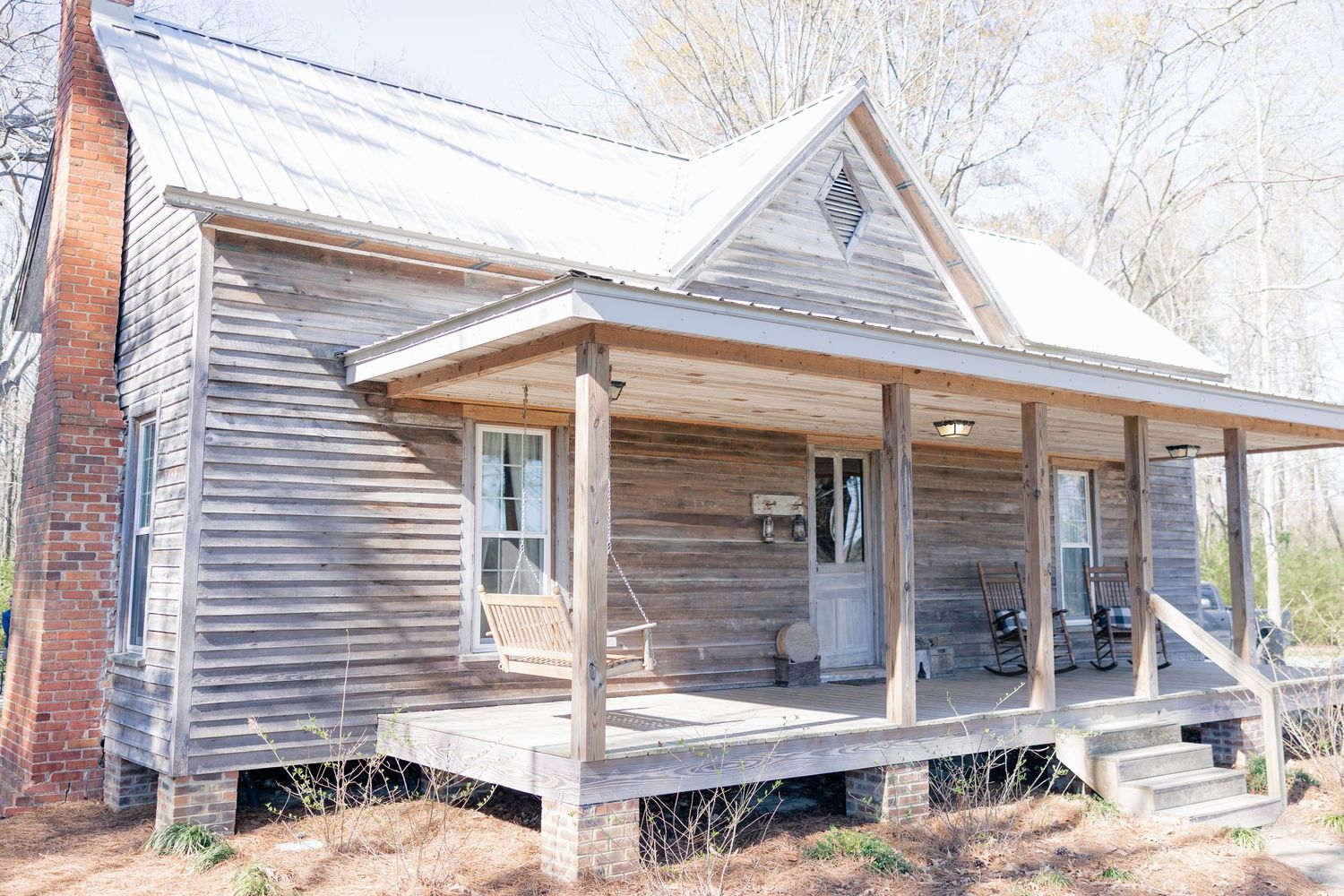 Row of rustic wooden cabin structures with covered porches stand weathered against a rural backdrop.