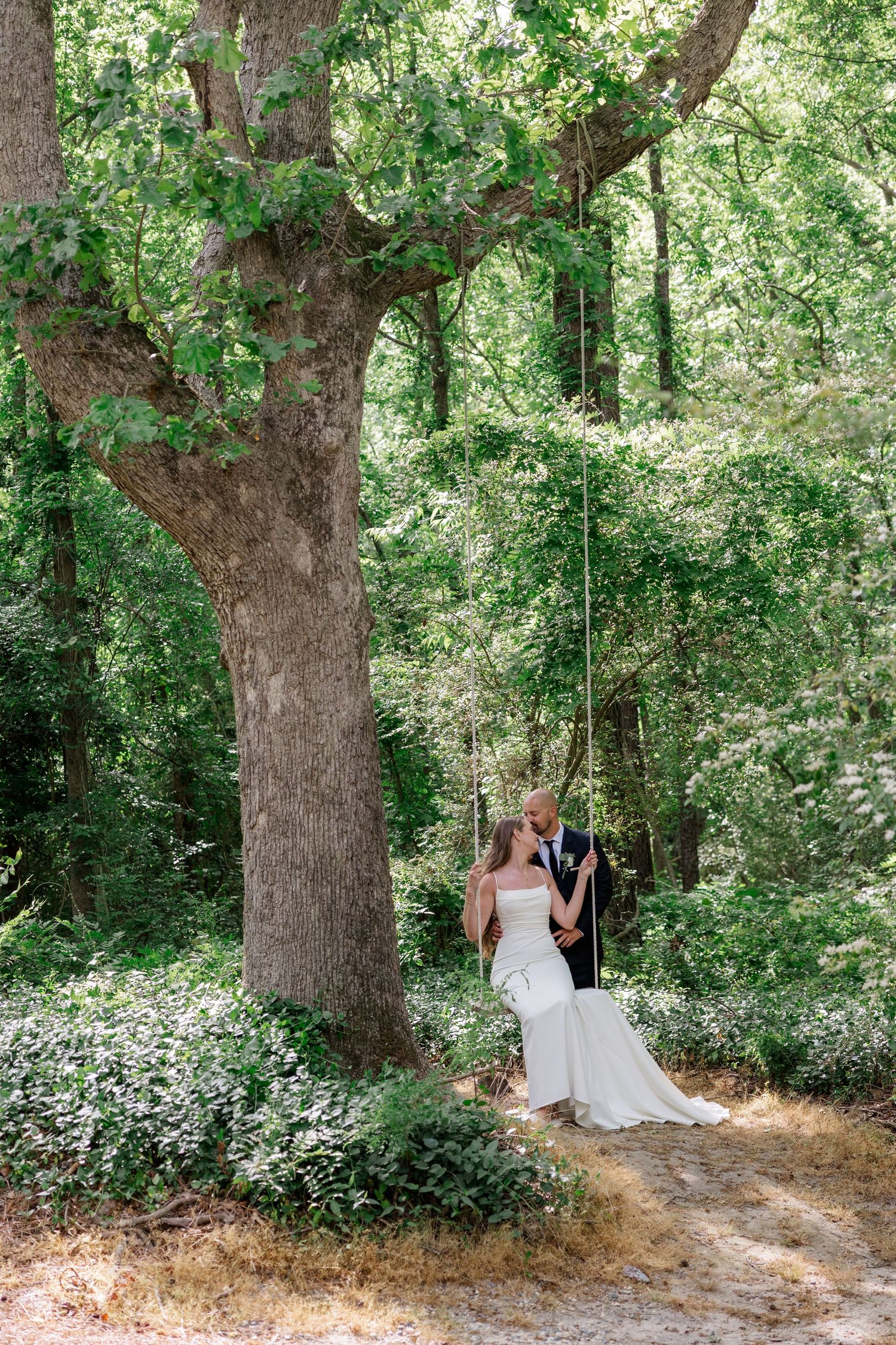 Wedding couple poses under large oak trees in a serene forest setting.