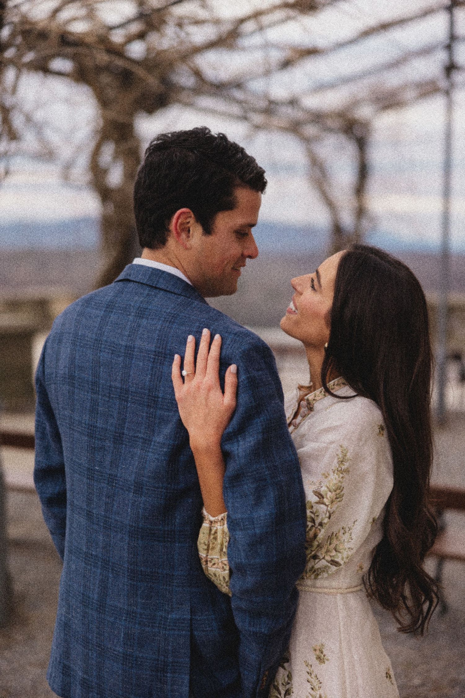 A romantic couple shares an intimate moment under a pergola, with the woman wearing a vintage-style dress with embroidery.