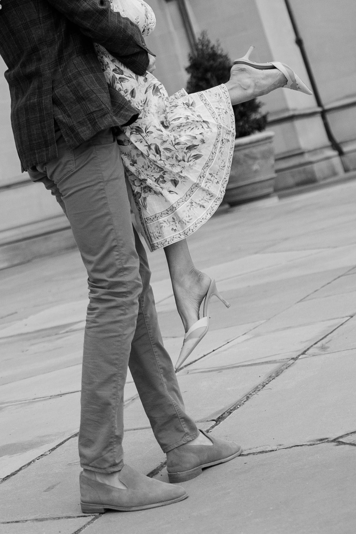 Black and white detail shot of dancing feet and flowing dress fabric against stone pavement.