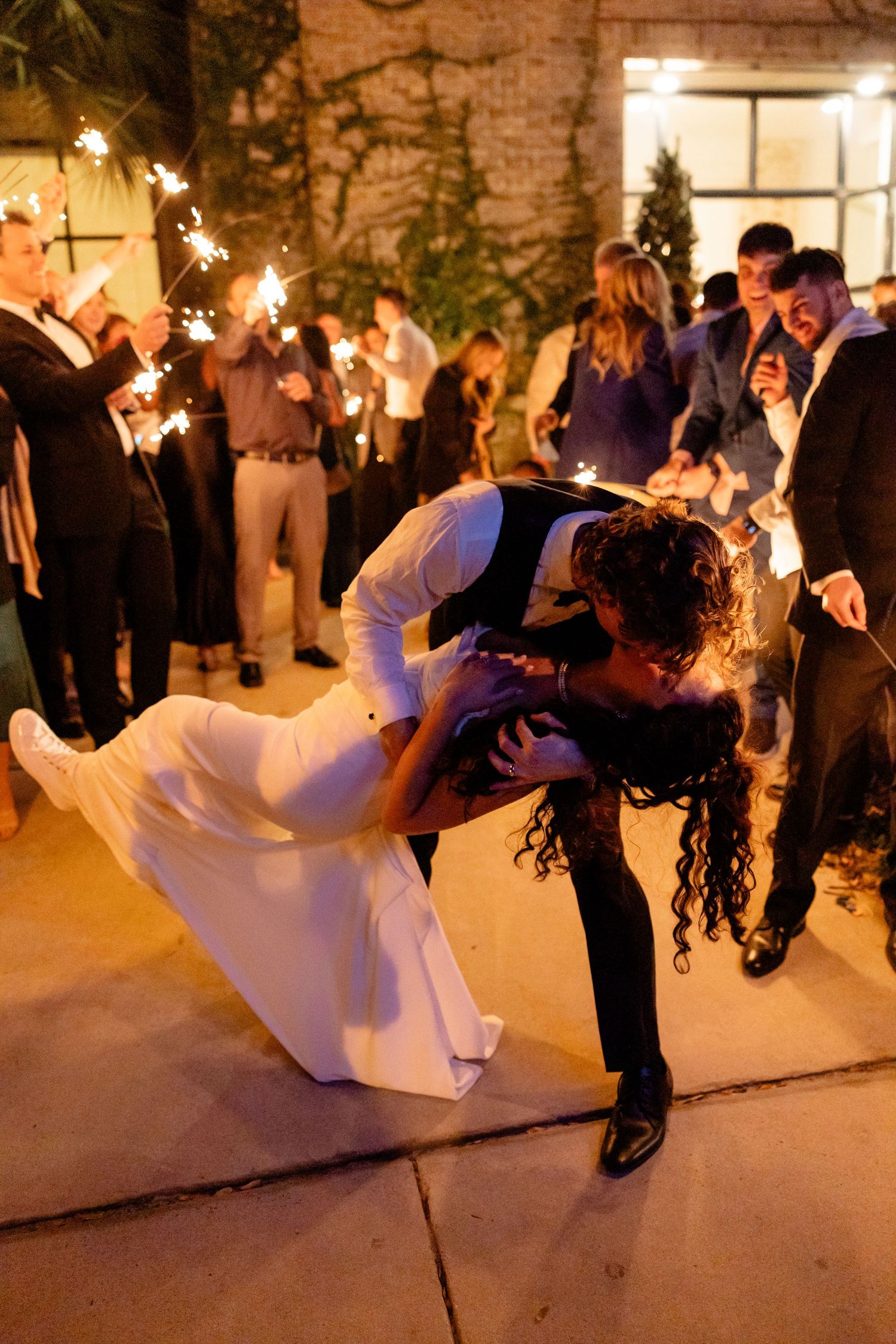 A romantic wedding reception sparkler exit with a dramatic dip kiss under twinkling lights.