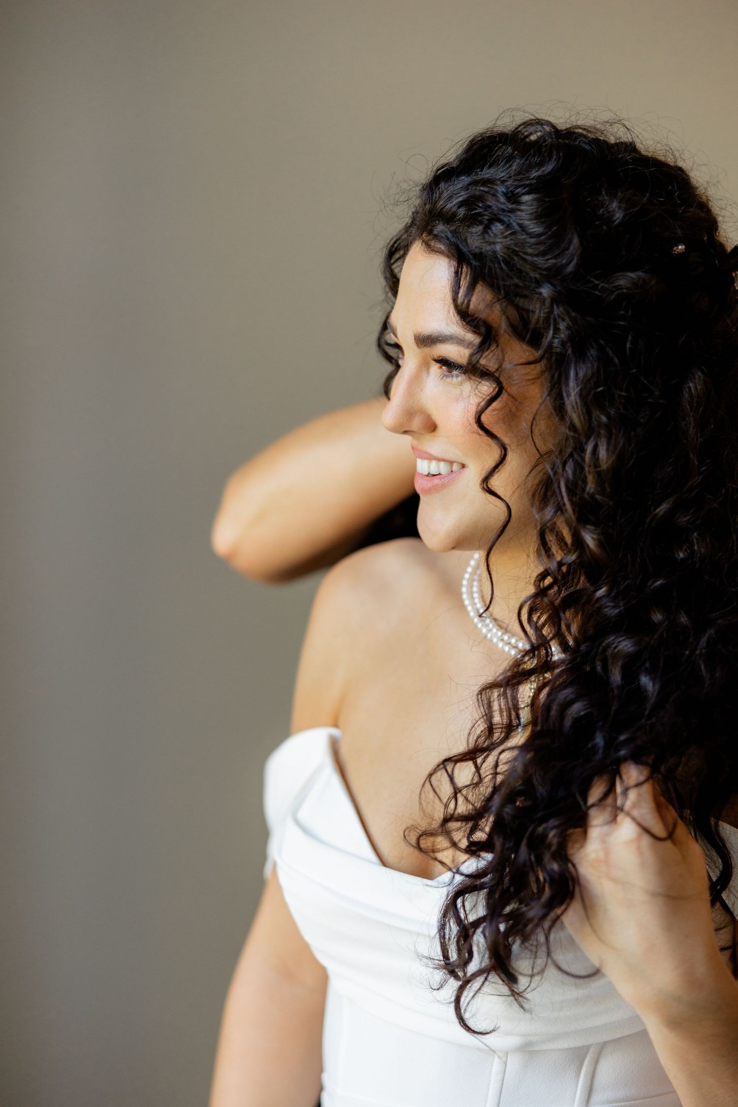A side profile of a bride wearing a white dress and diamond earrings with long dark curly hair.