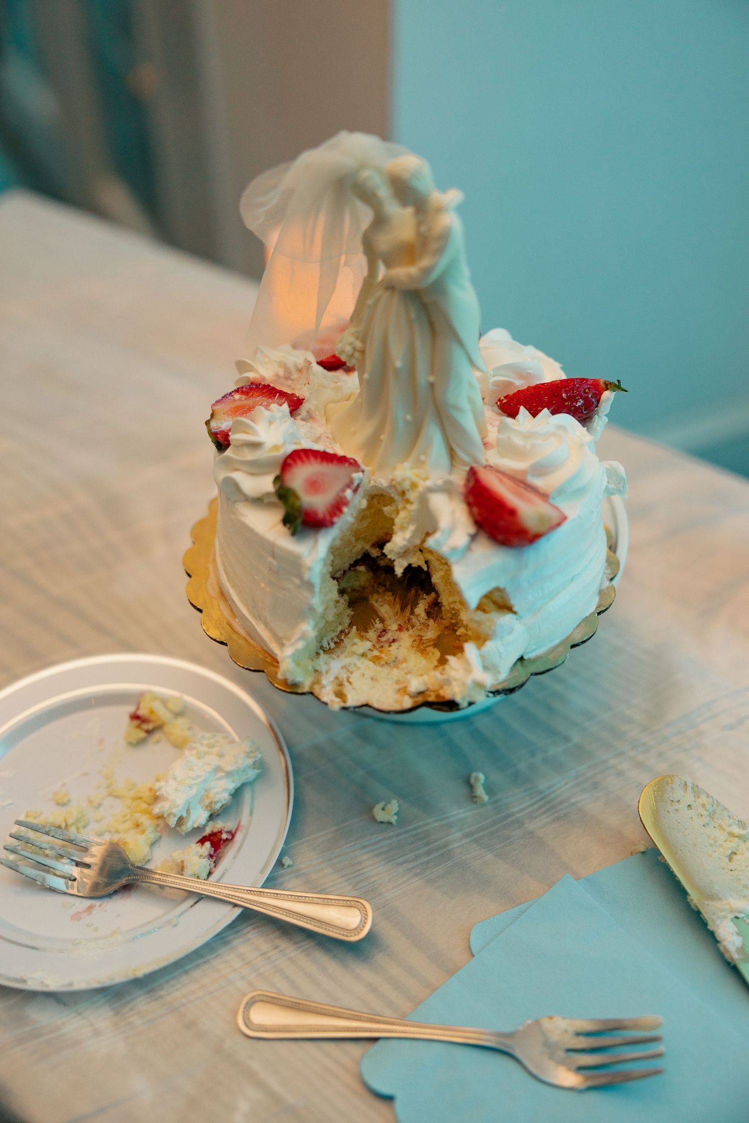 Partially cut white wedding cake decorated with strawberries and whipped cream frosting.