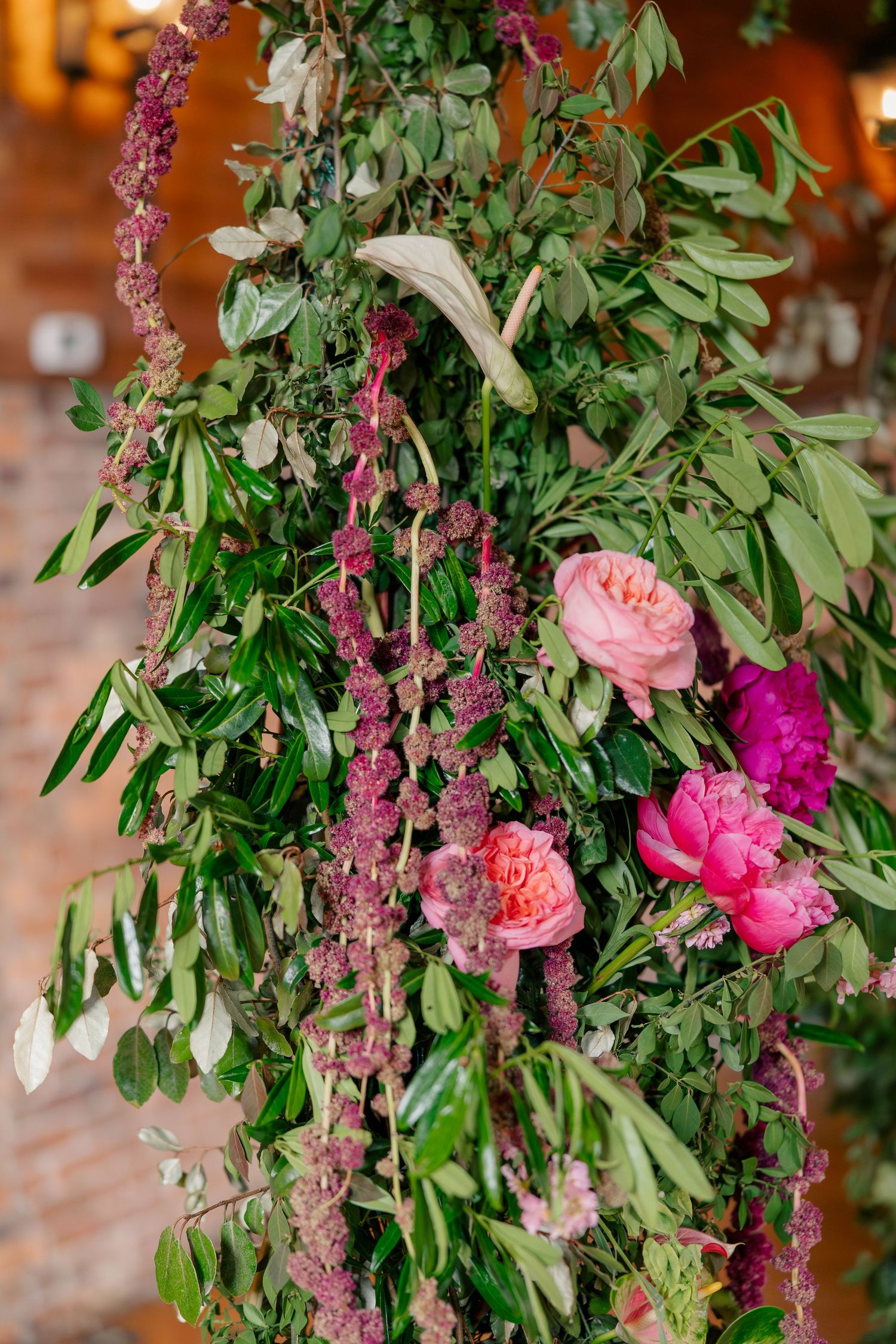 Lush floral wedding arch with pink peonies, roses, and cascading greenery in rustic venue.