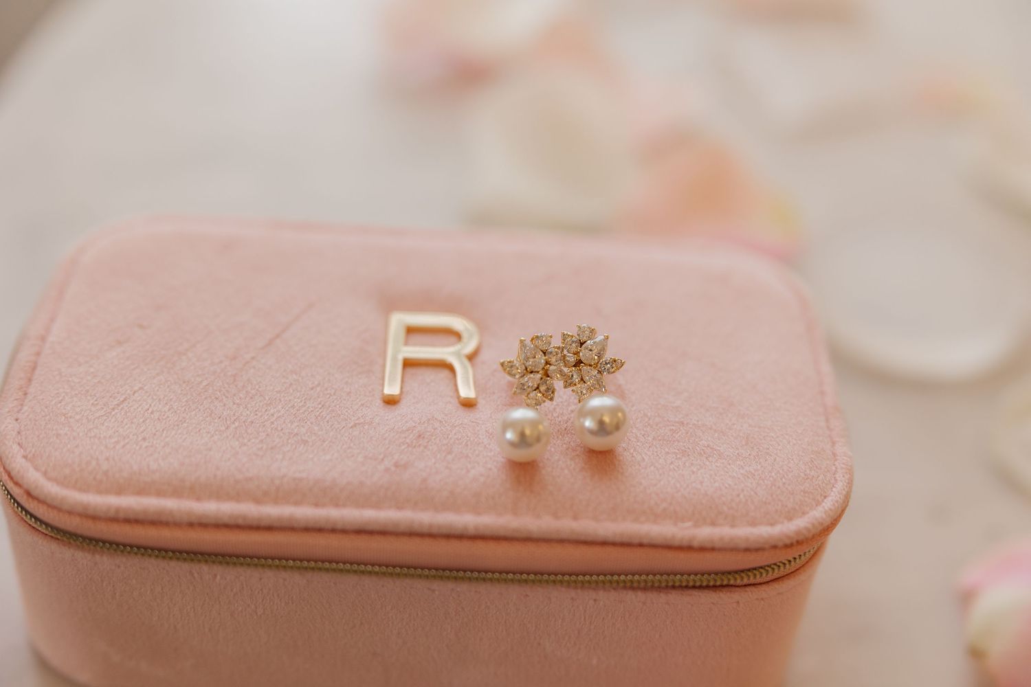 Gold letter R and delicate star earrings displayed on a pink jewelry case with soft blurred background.