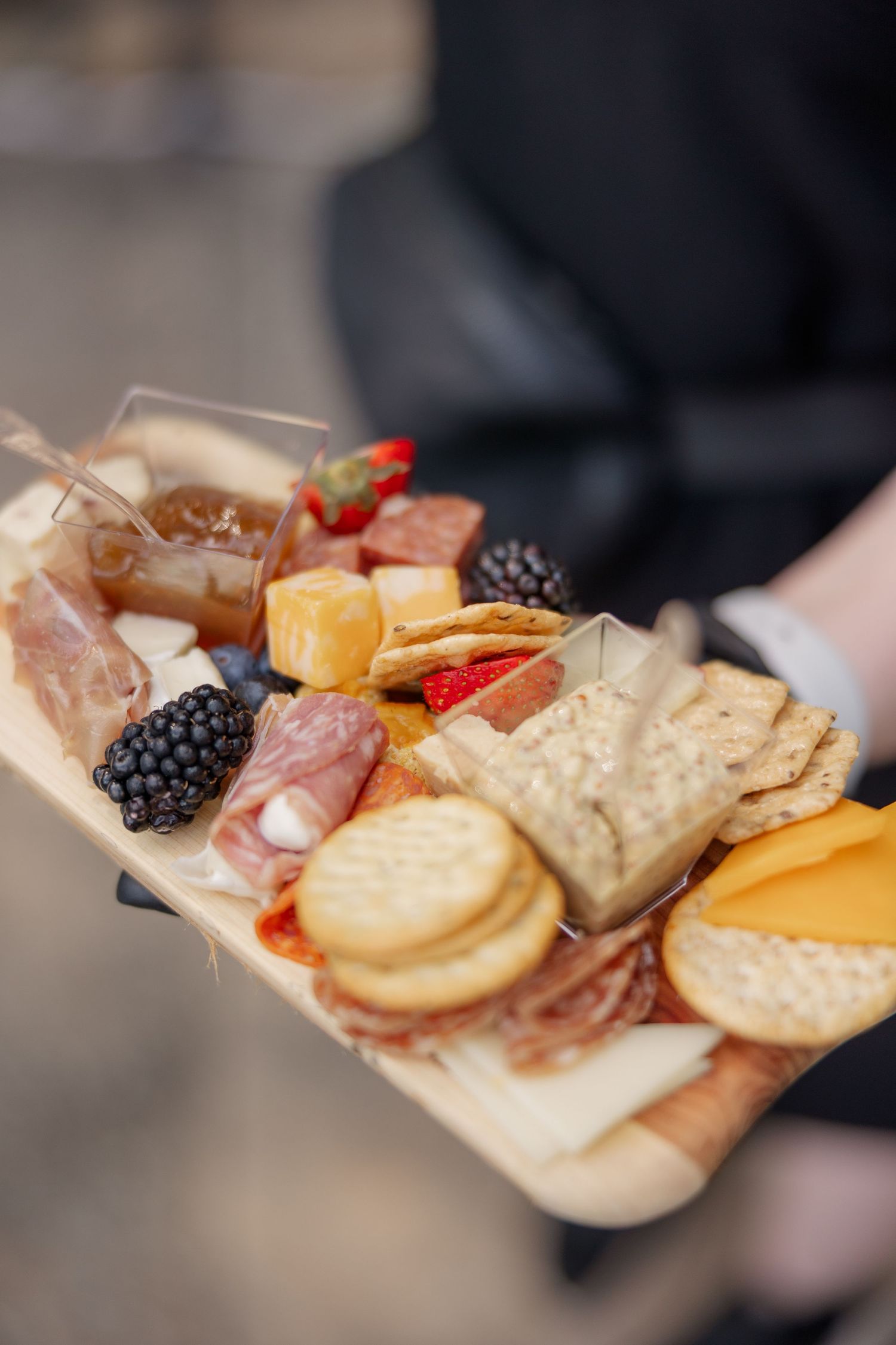 A charcuterie board with meats, cheeses, fruits and crackers displayed on a wooden platter.