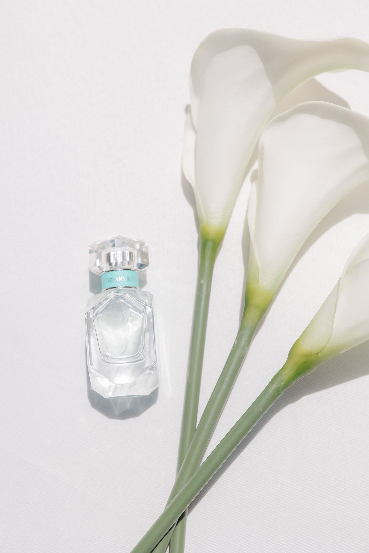 Elegant perfume bottle displayed with white calla lilies against white background.