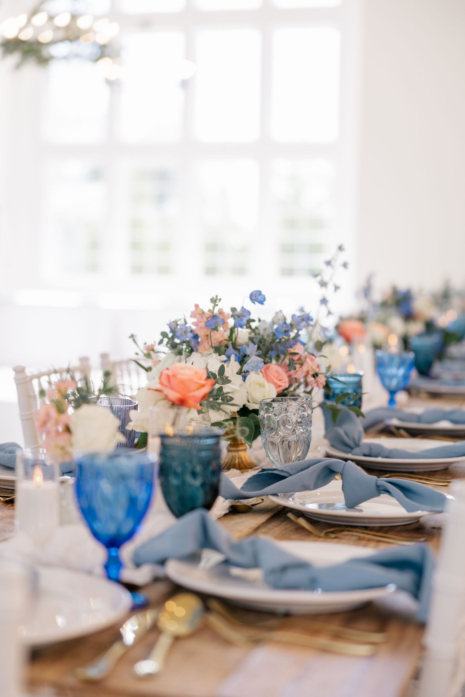 Wedding reception tables with blue and white place settings, floral centerpieces and gold accents.