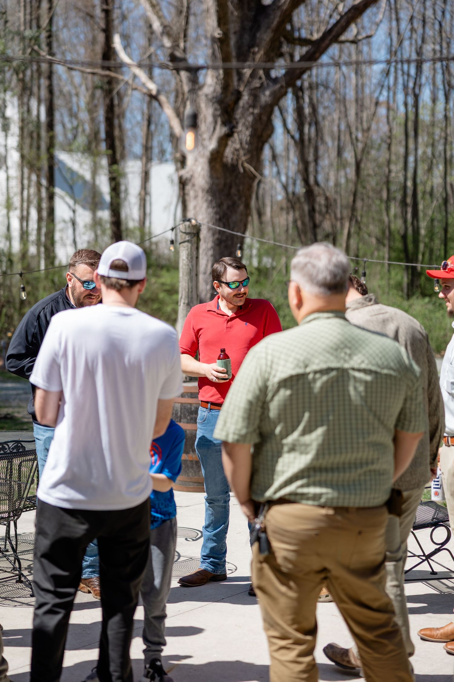 A group of guests gathering outdoors near wooded trees during a daytime event.