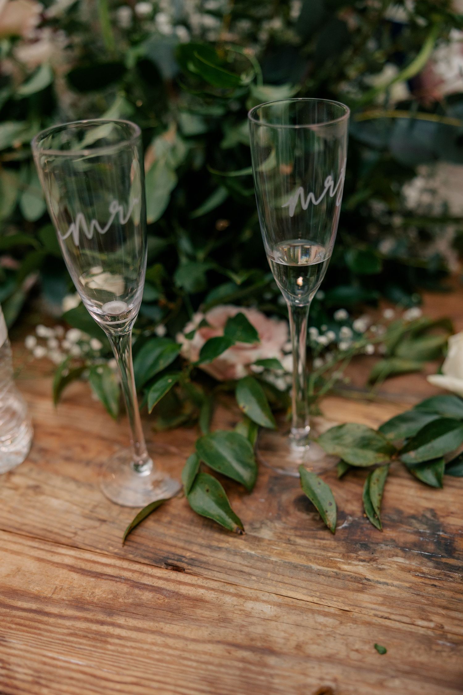 Empty champagne glasses arranged on a wooden table with decorative greenery for a wedding celebration.