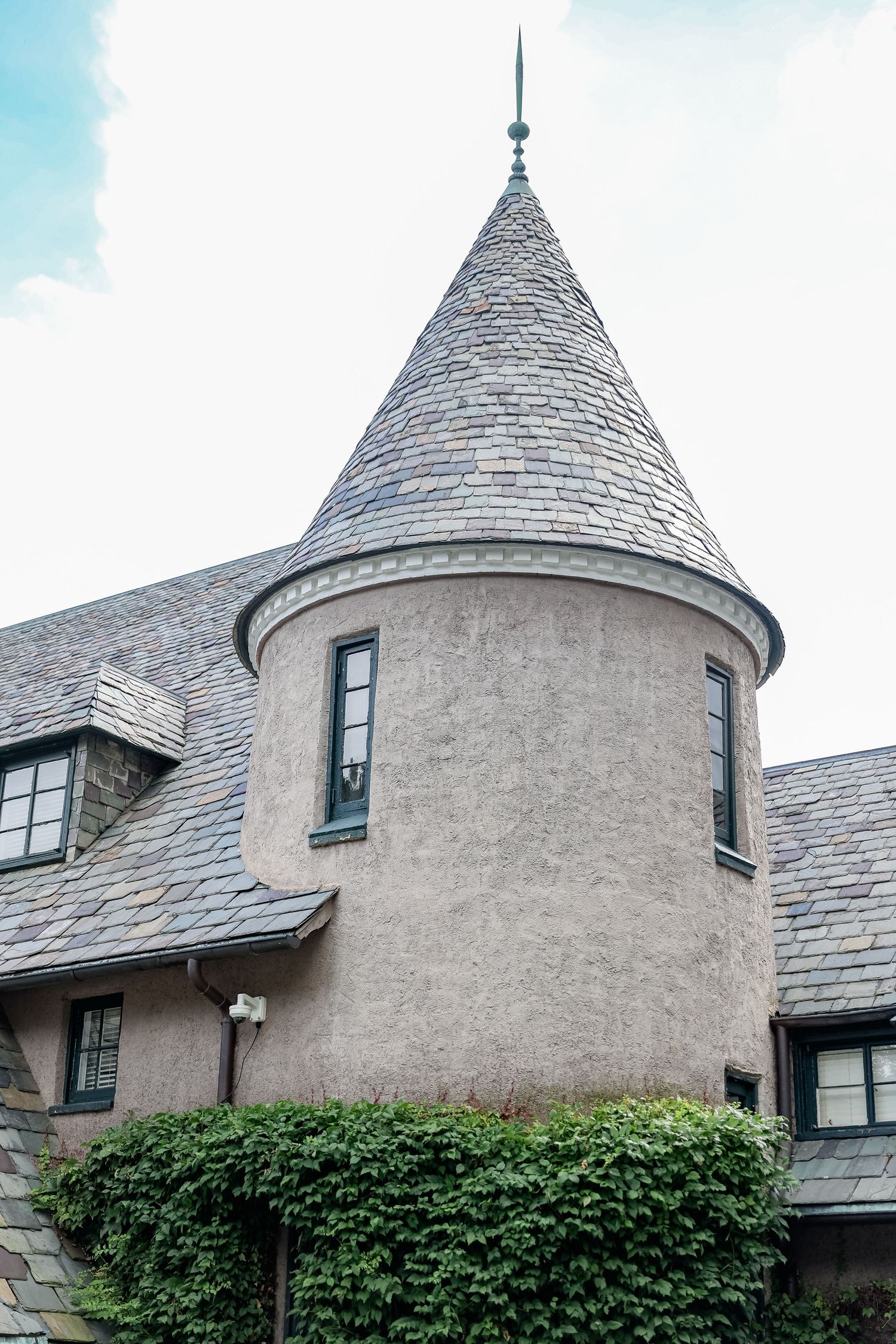 Architectural details of a modern castle-like building with multiple turrets and gray stucco walls covered in climbing ivy.