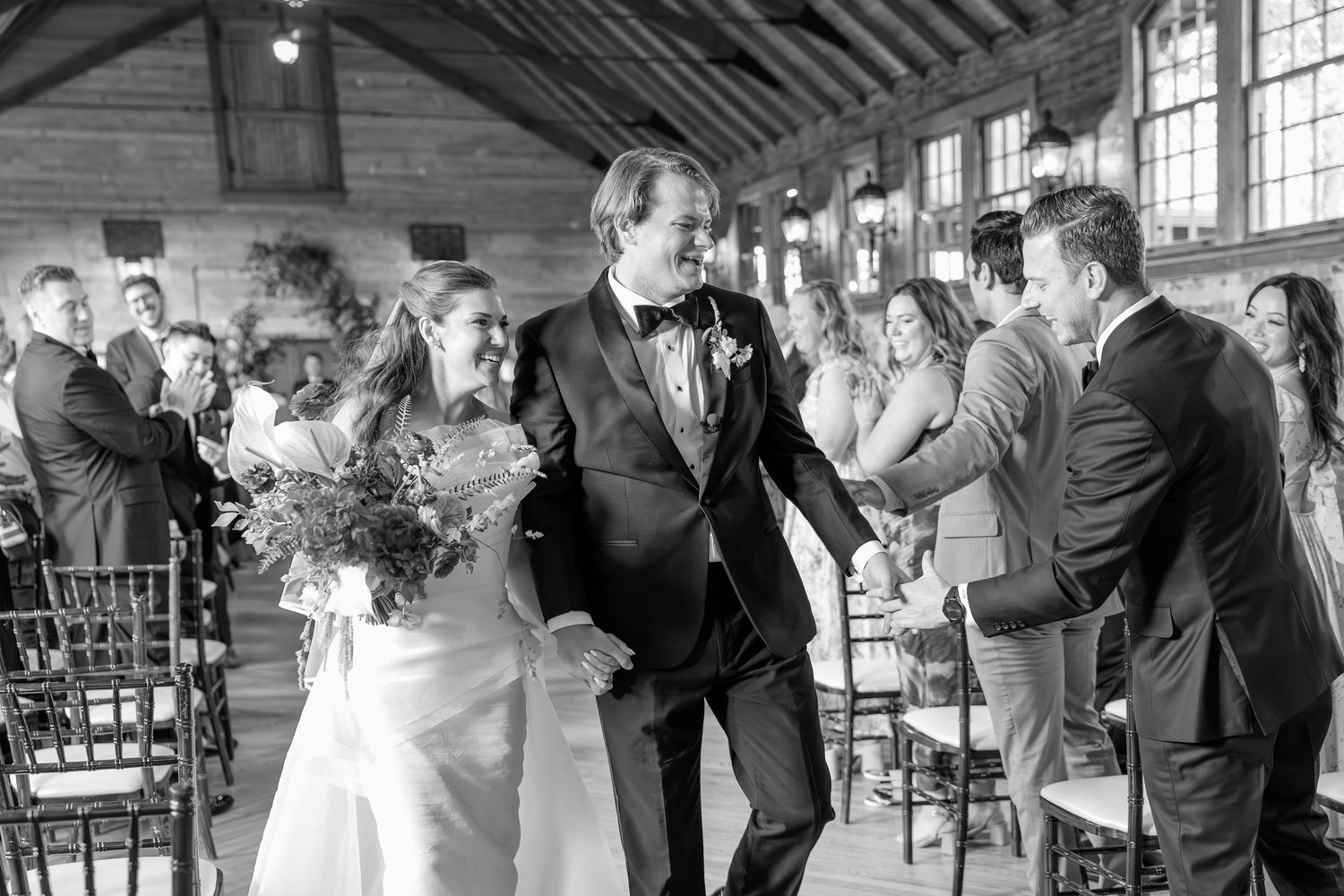 Black and white photo of a joyful bride and groom walking down the aisle after their wedding ceremony.
