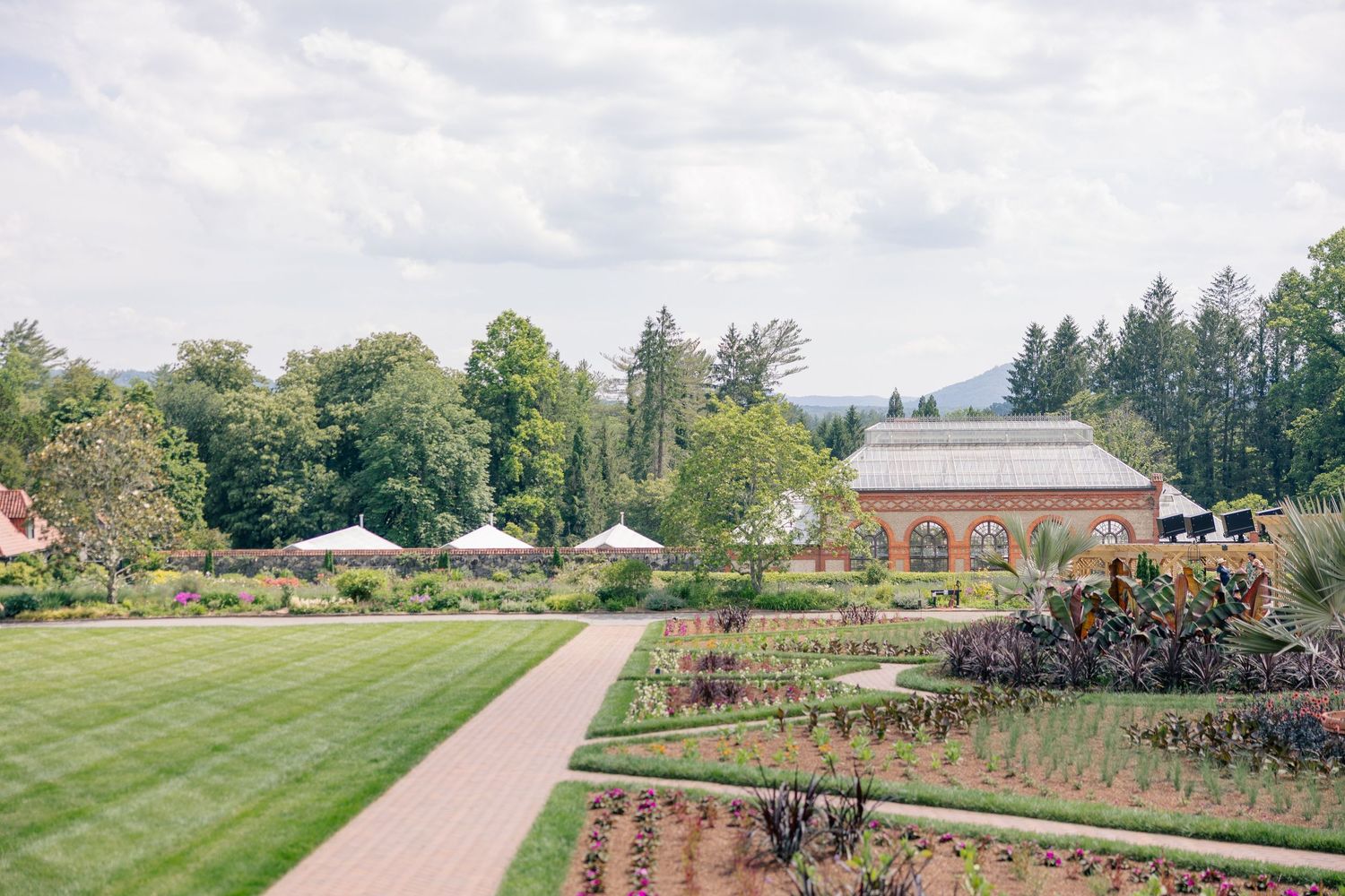 Elegant wedding venue with manicured gardens, greenhouse, and white tent on a cloudy summer day.