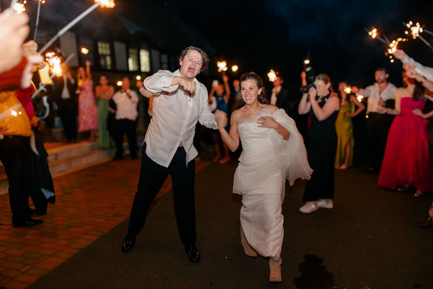 Bride and groom celebrating sparkler exit with cheering guests lining the path at night reception.