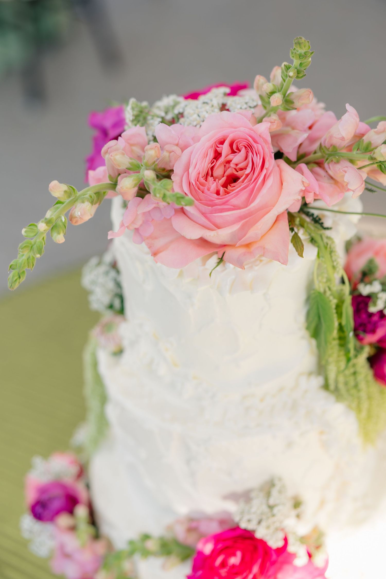 Three-tier white wedding cake topped with pink garden roses and greenery floral accents.