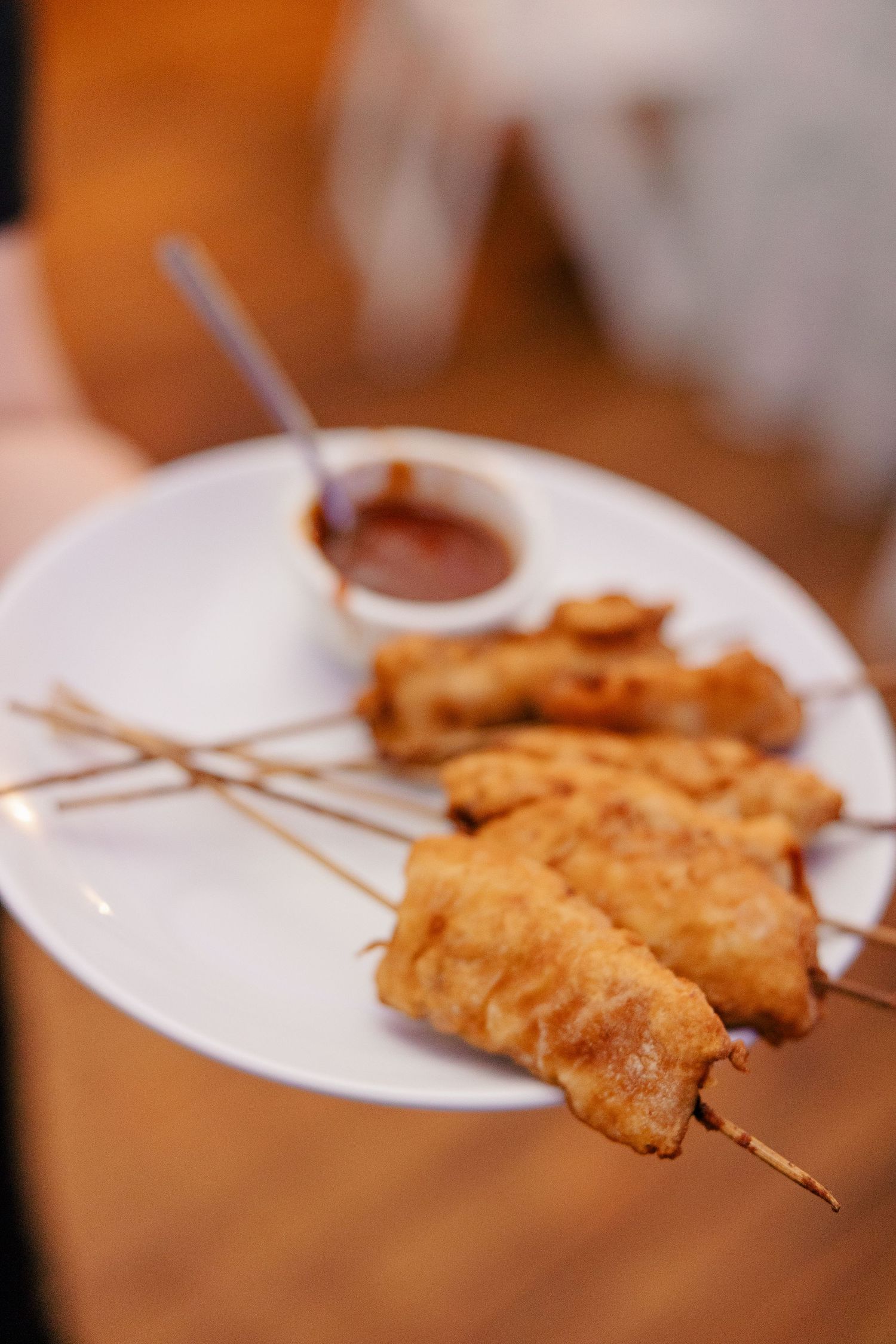 Golden fried chicken skewers served on a white plate with a small bowl of dipping sauce.