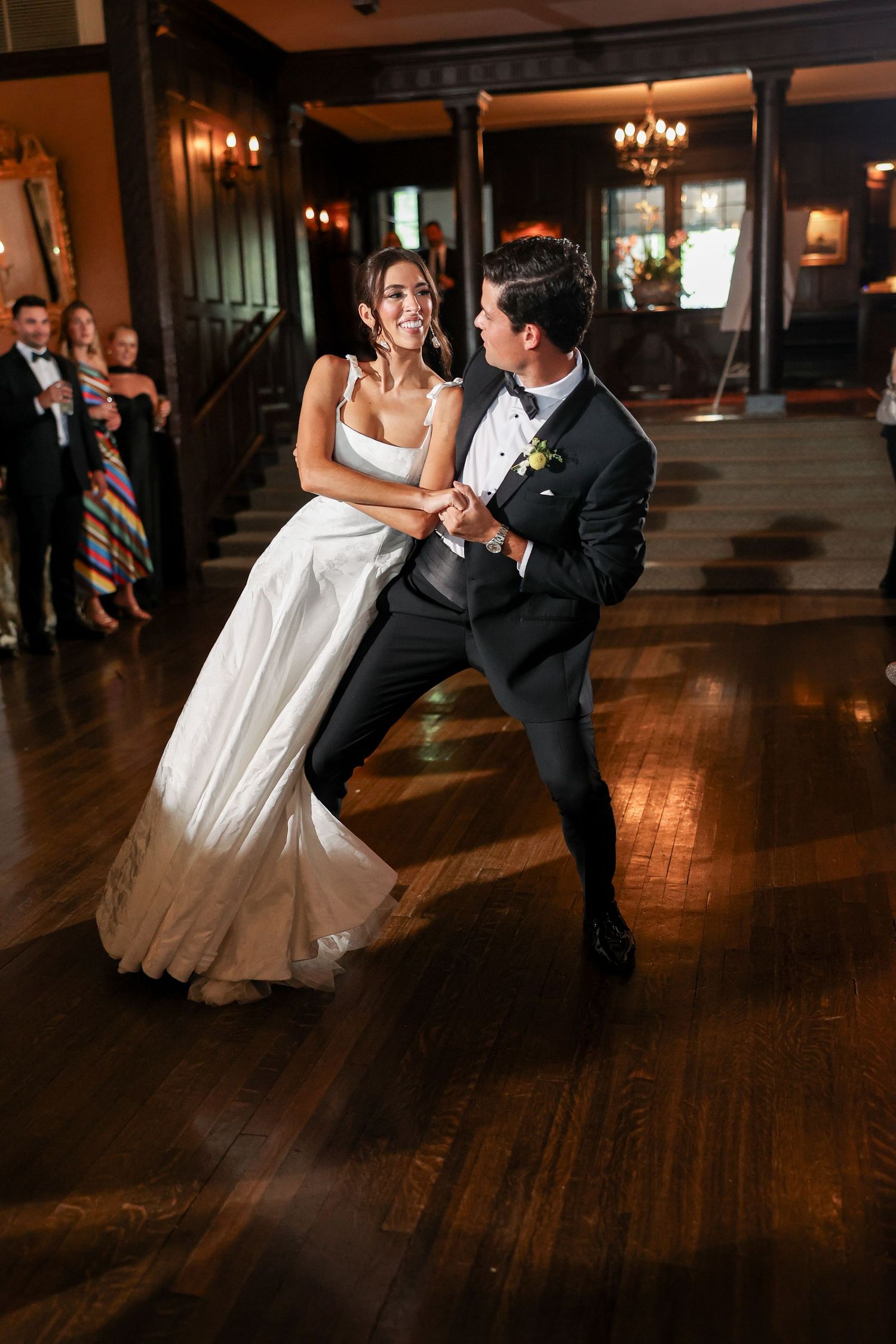 Bride and groom share their first dance on a wooden dance floor at an elegant wedding reception.