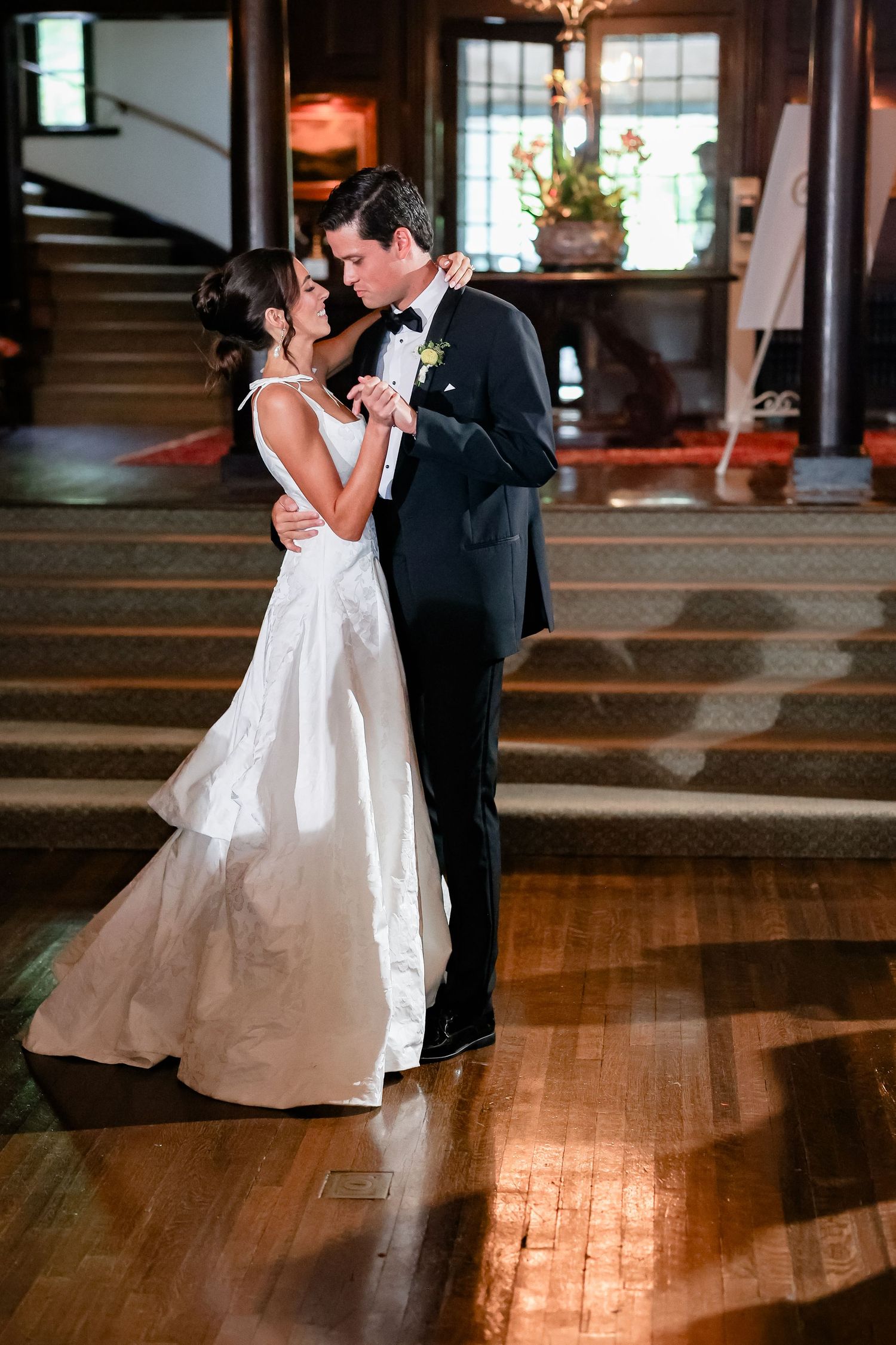 Bride and groom share romantic first dance in stunning white gown and black tuxedo in historic venue.