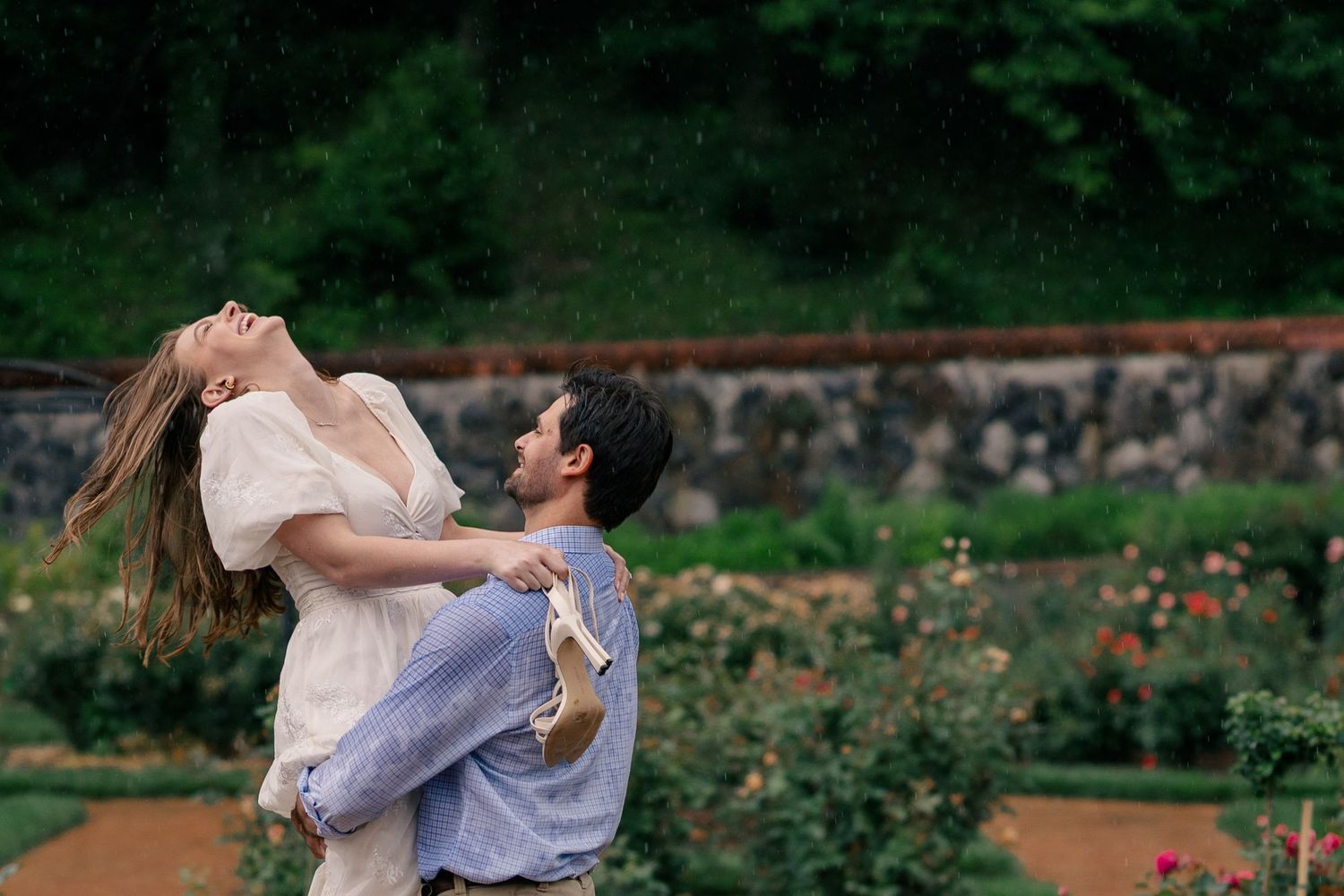 A couple dancing in a rustic garden scenery with stone walls and green trees in the background.
