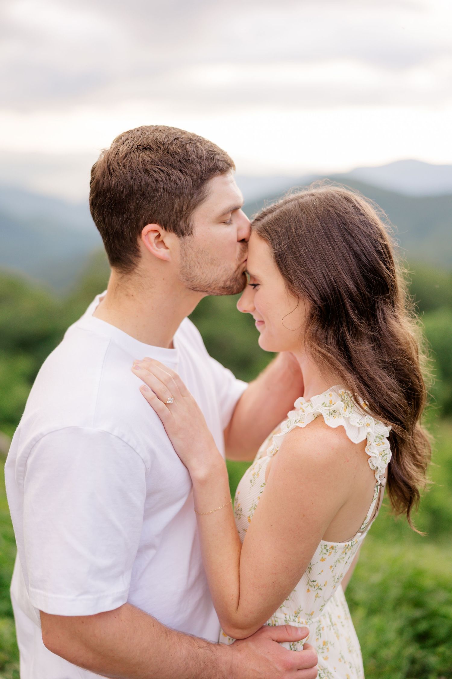 A tender moment between a couple in white clothing as they share an intimate embrace with mountains in the background.