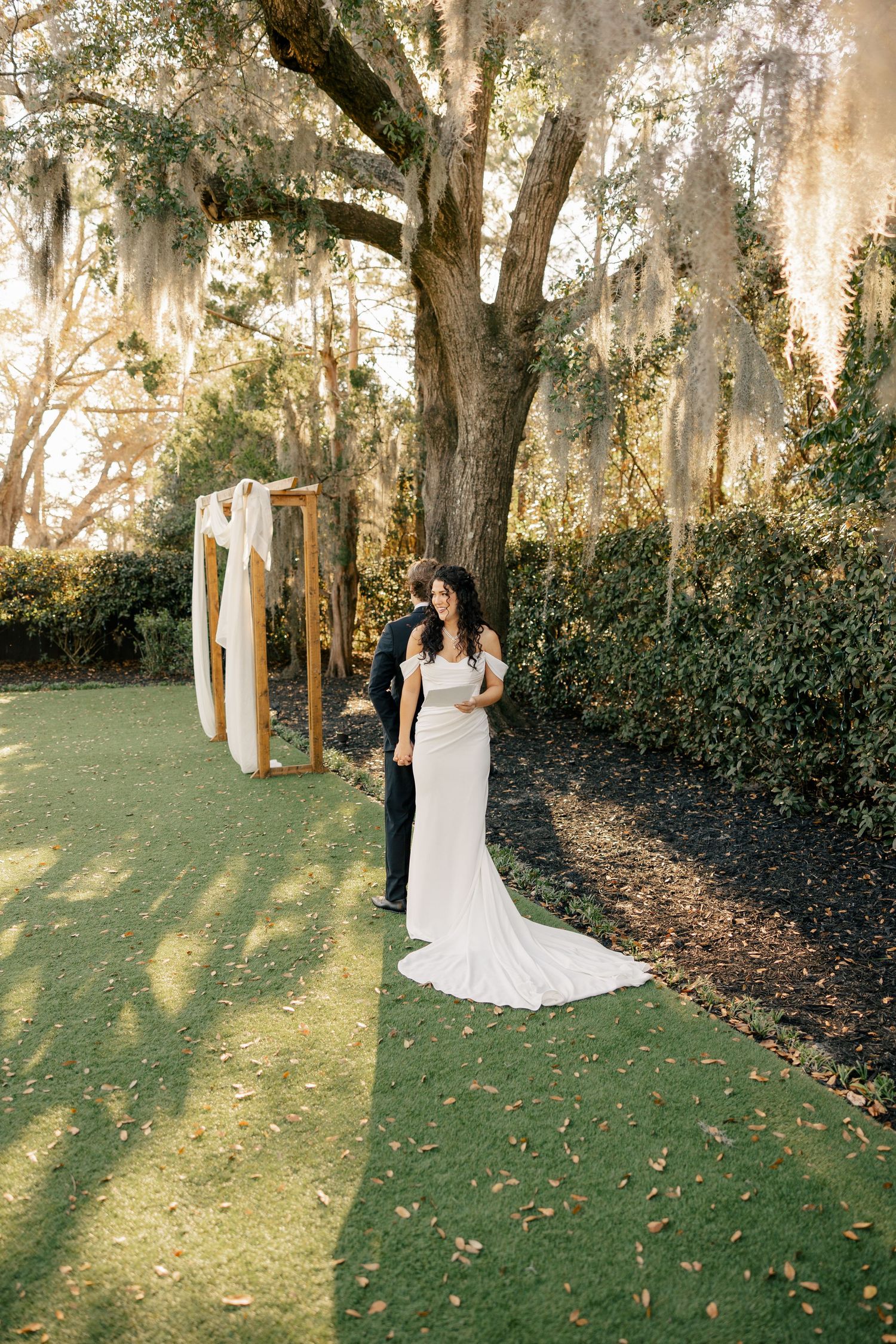 A white wedding dress is displayed against a dreamy backdrop of Spanish moss draped trees at sunset.