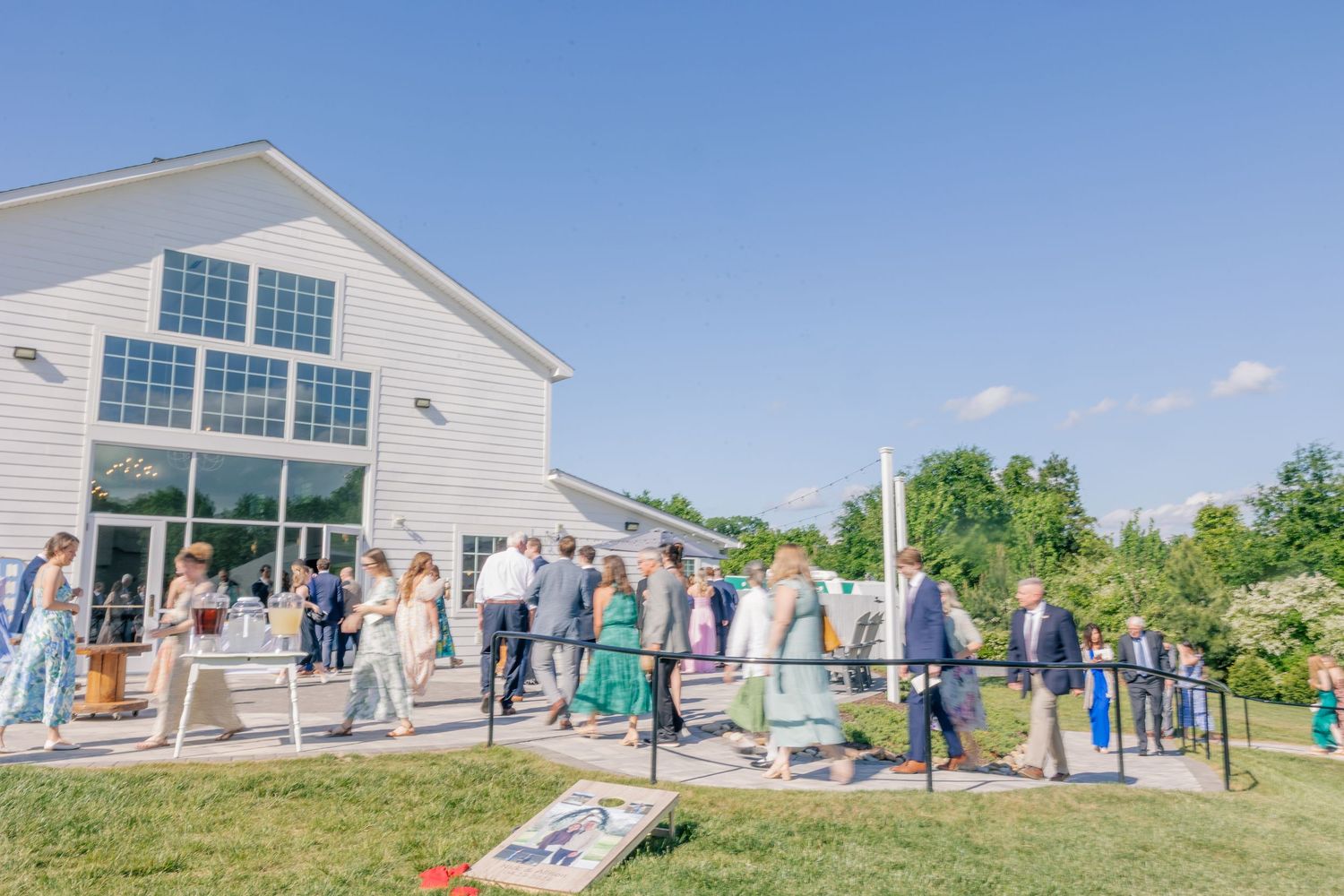 Wedding guests mingling outside a white barn venue on a sunny summer wedding day.
