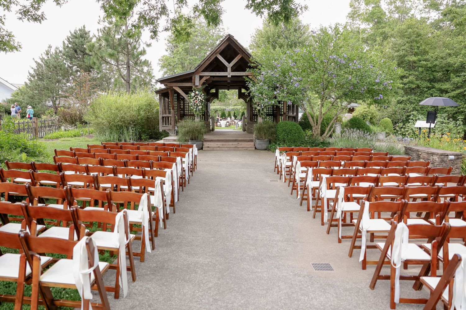 Rustic wooden wedding ceremony setup with rows of brown chairs and white cushions leading to a timber pergola.