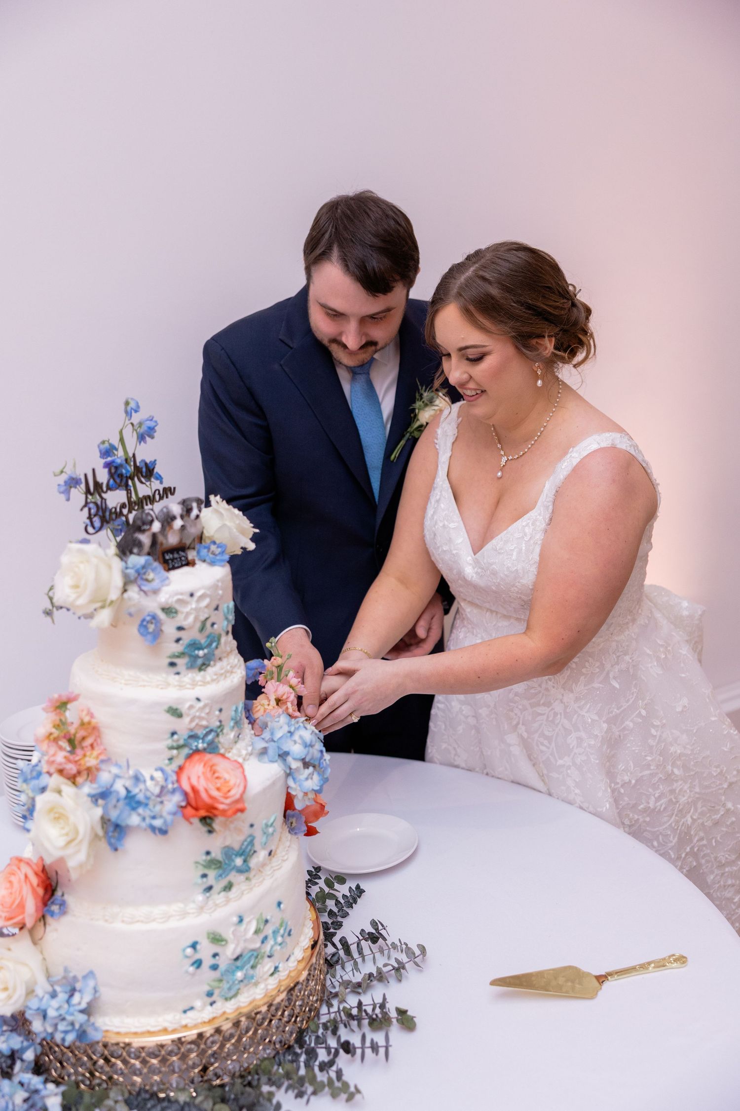 A couple cuts their wedding cake decorated with blue and peach flowers at their reception.