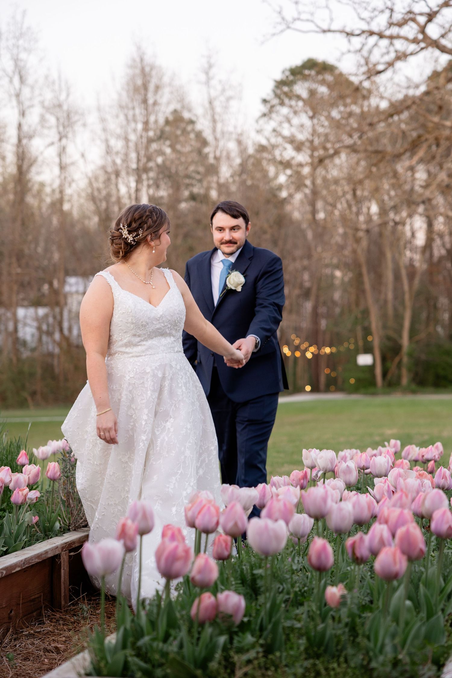 A couple shares a romantic moment among blooming pink tulips in a garden setting during springtime.