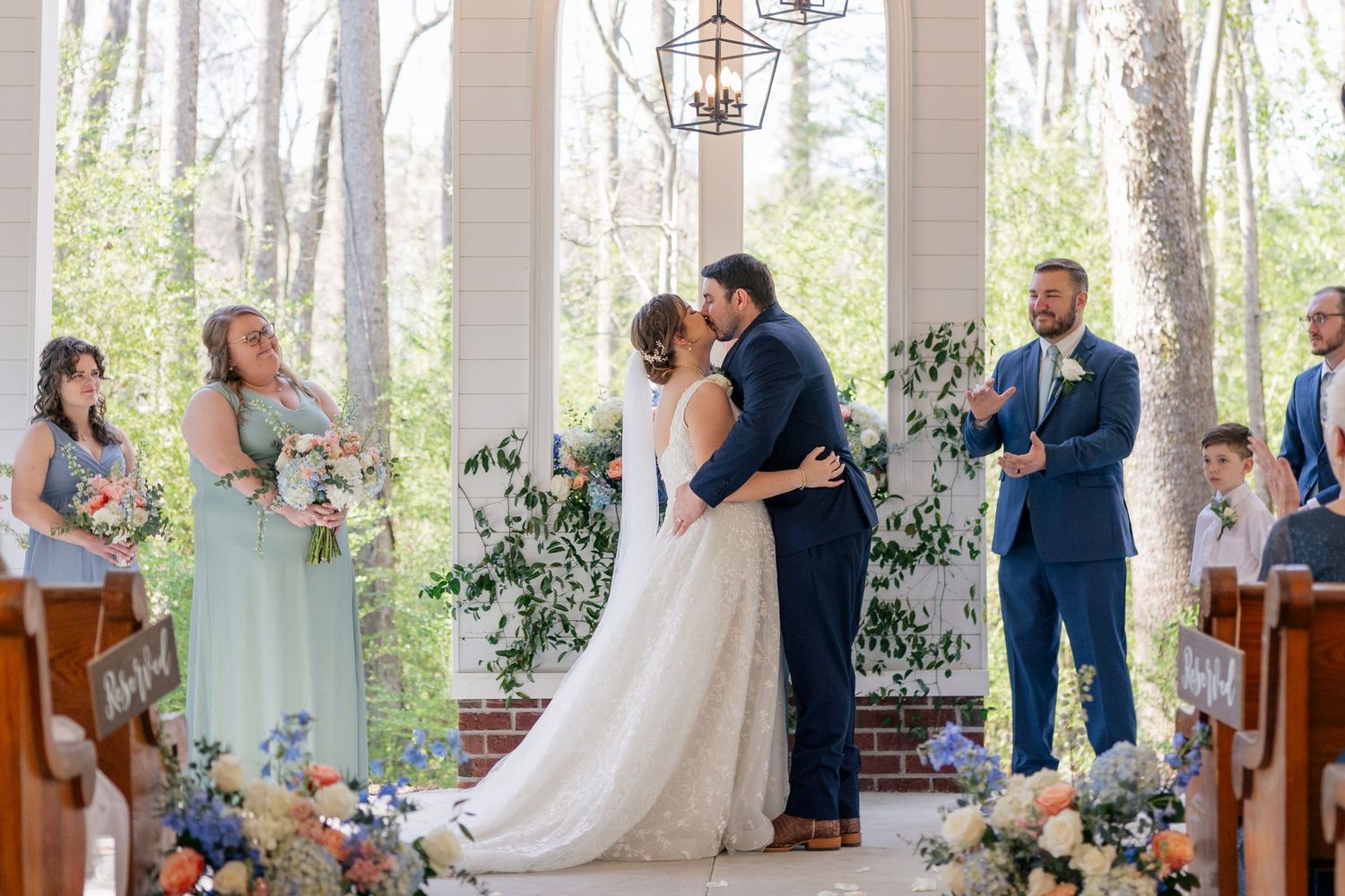 A wedding ceremony in a forest chapel with floral decorations and guests watching the couple exchange vows.