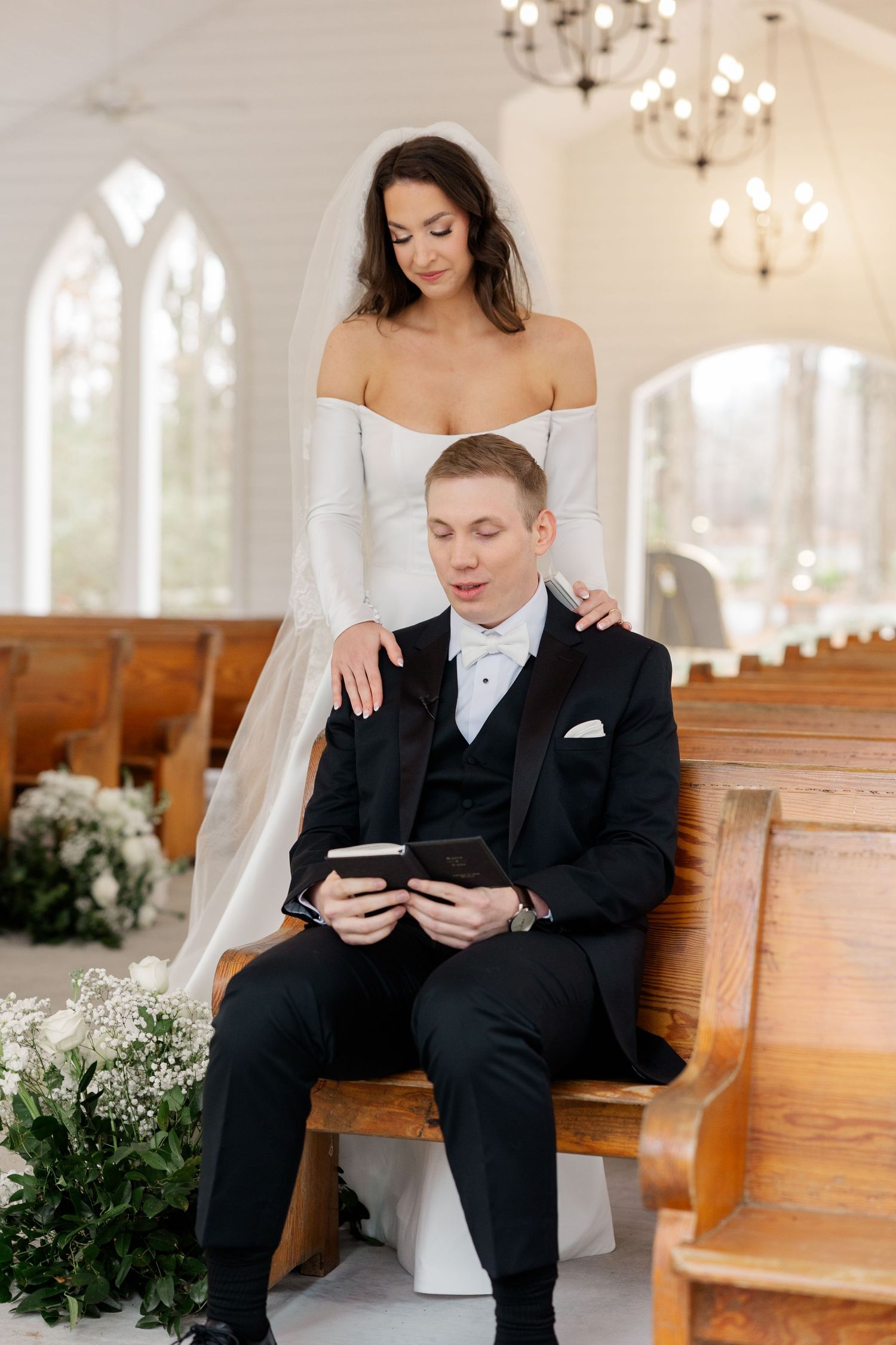 An intimate moment captured in a chapel with wooden pews and chandelier lighting.