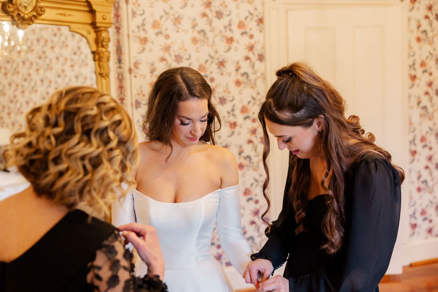 Wedding preparations taking place in an elegant room with floral wallpaper.