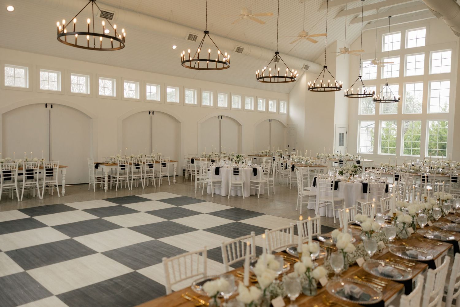 Elegant white wedding reception hall with checkered floor and crystal chandeliers.