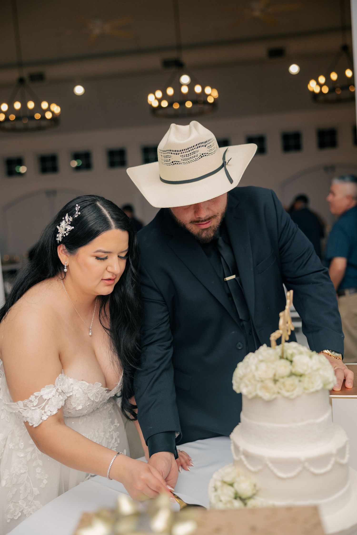 Couple in western-themed wedding attire cut their elegant white wedding cake together.