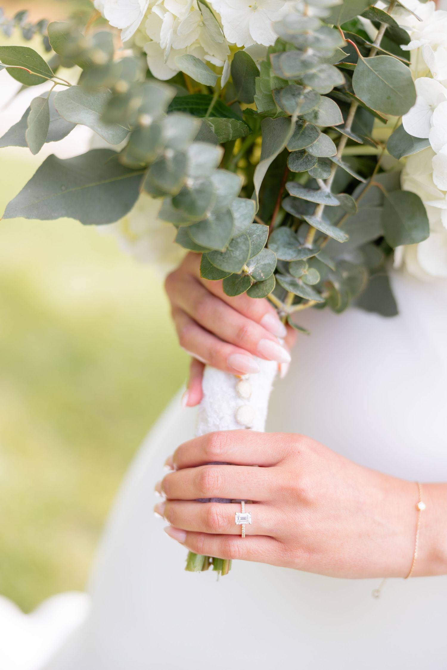 Close-up view of hands holding a white floral bouquet with an elegant engagement ring on display.