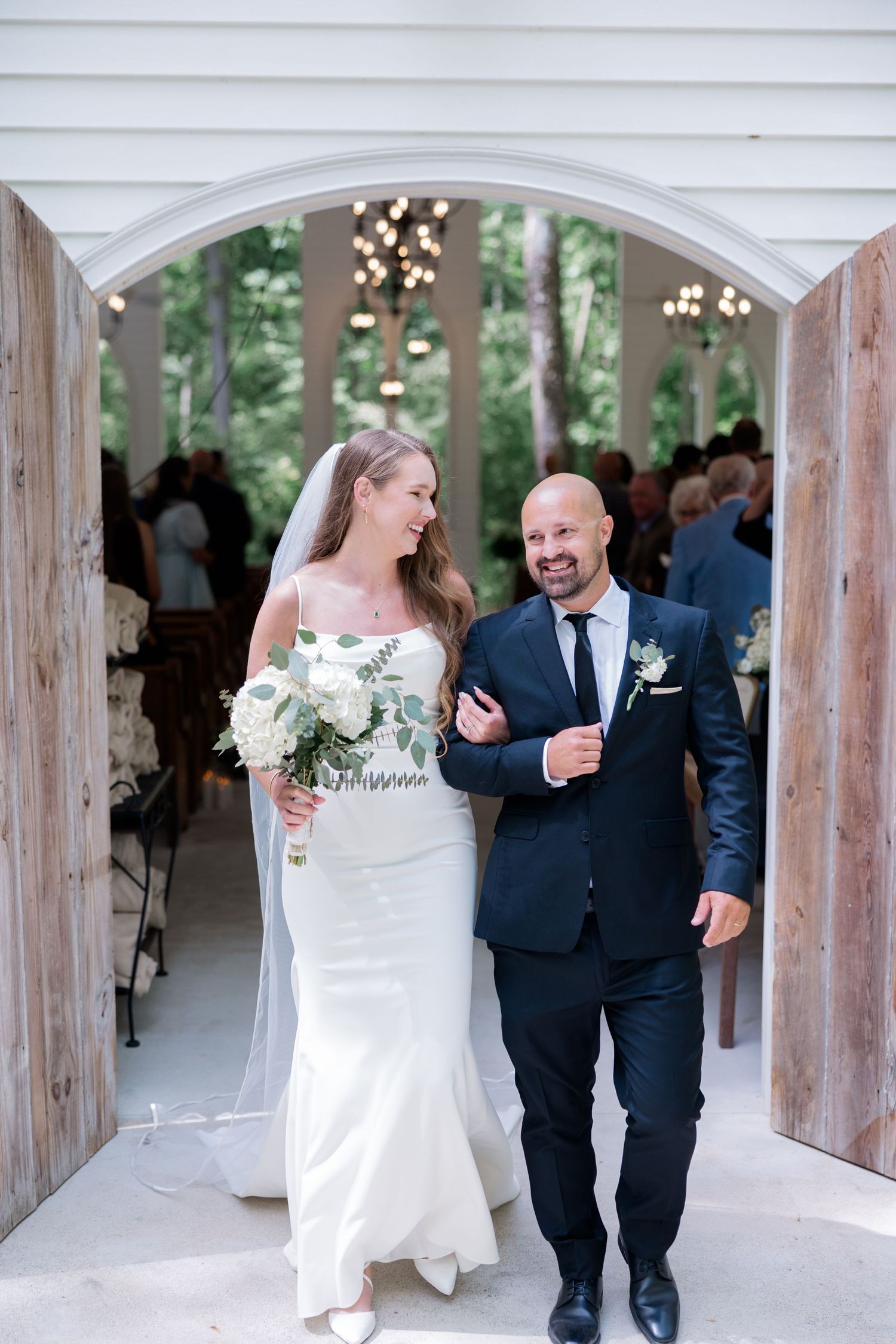 Newlyweds share a joyful exit walk under an elegant white archway after their wedding ceremony.