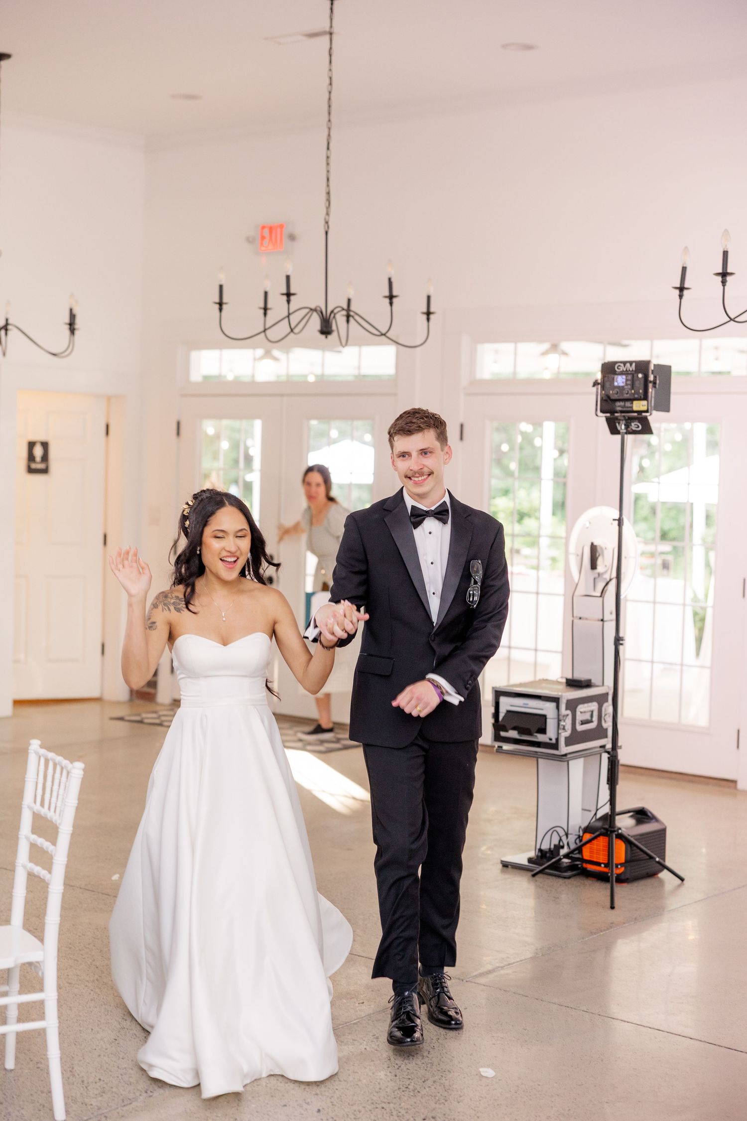 Couple in wedding attire dancing and celebrating in an elegant white reception venue with black and white floor.