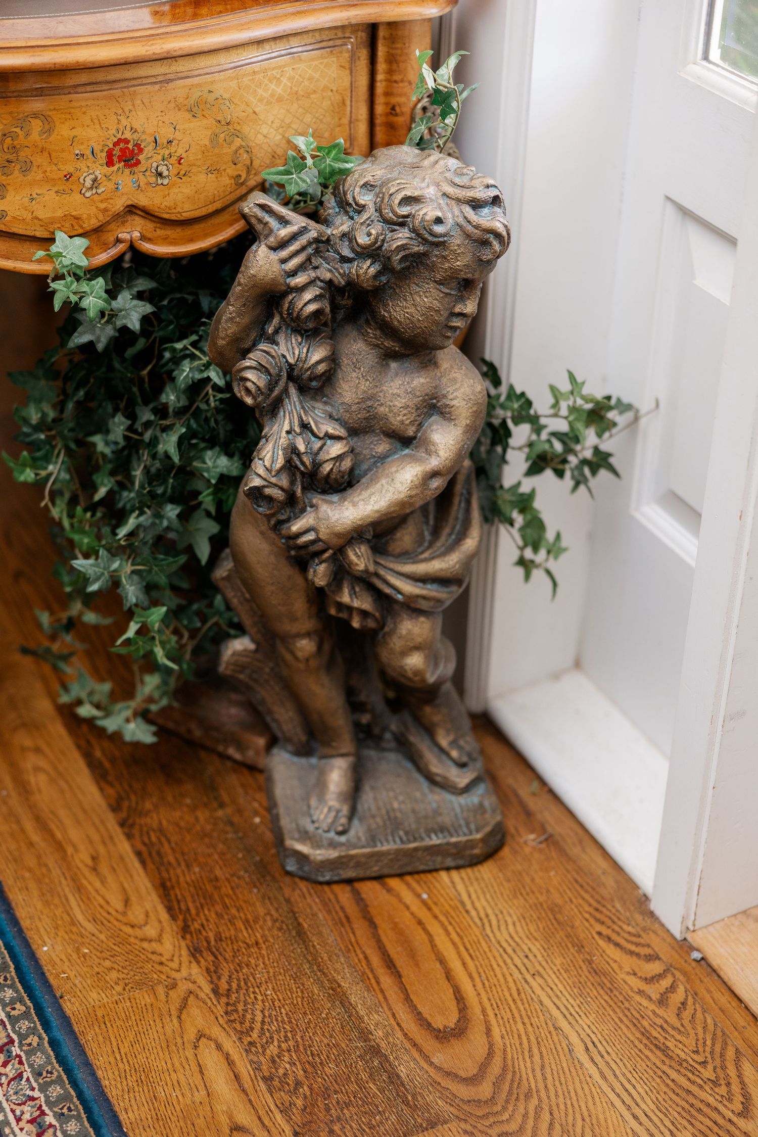Decorative bronze cherub statue sits in corner of room with hardwood floors and white walls.