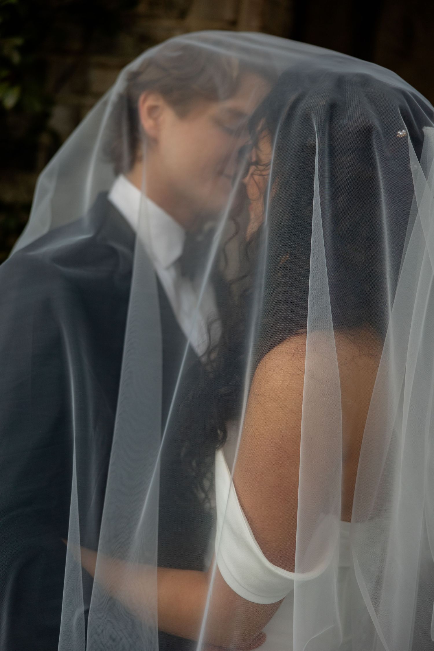 A romantic wedding moment captured through a sheer white veil as a couple shares an intimate kiss.
