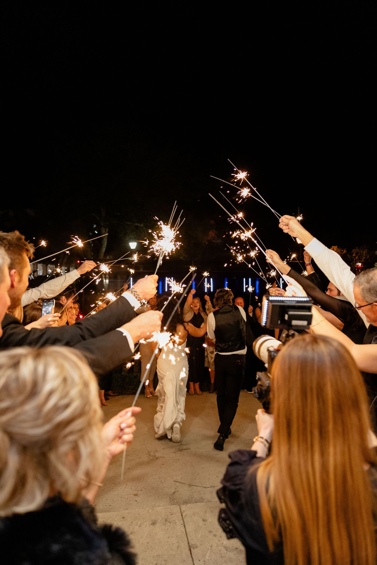 Wedding guests hold sparklers creating a magical tunnel exit for celebration.