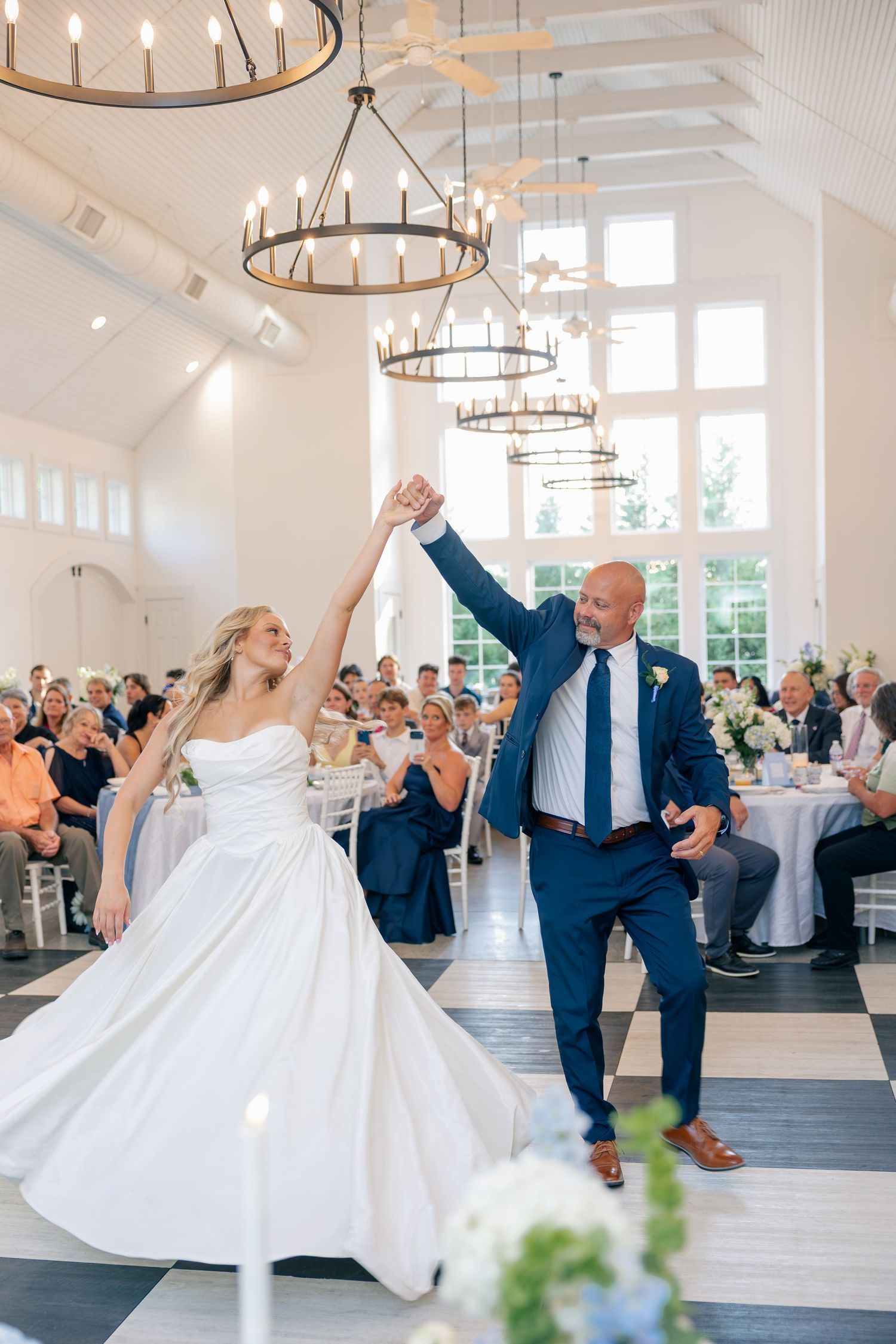 Bride and man in navy suit twirl together on checkered dance floor during wedding reception.