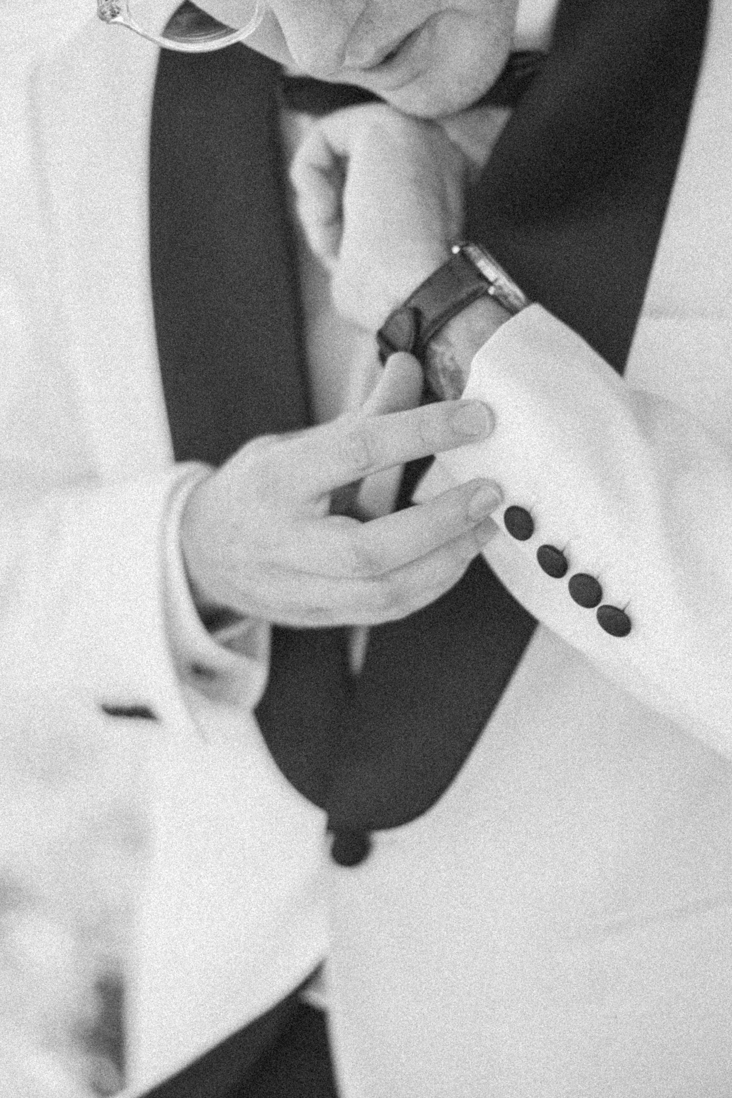 Black and white close-up of groom in white tuxedo jacket fastening his watch cufflink.