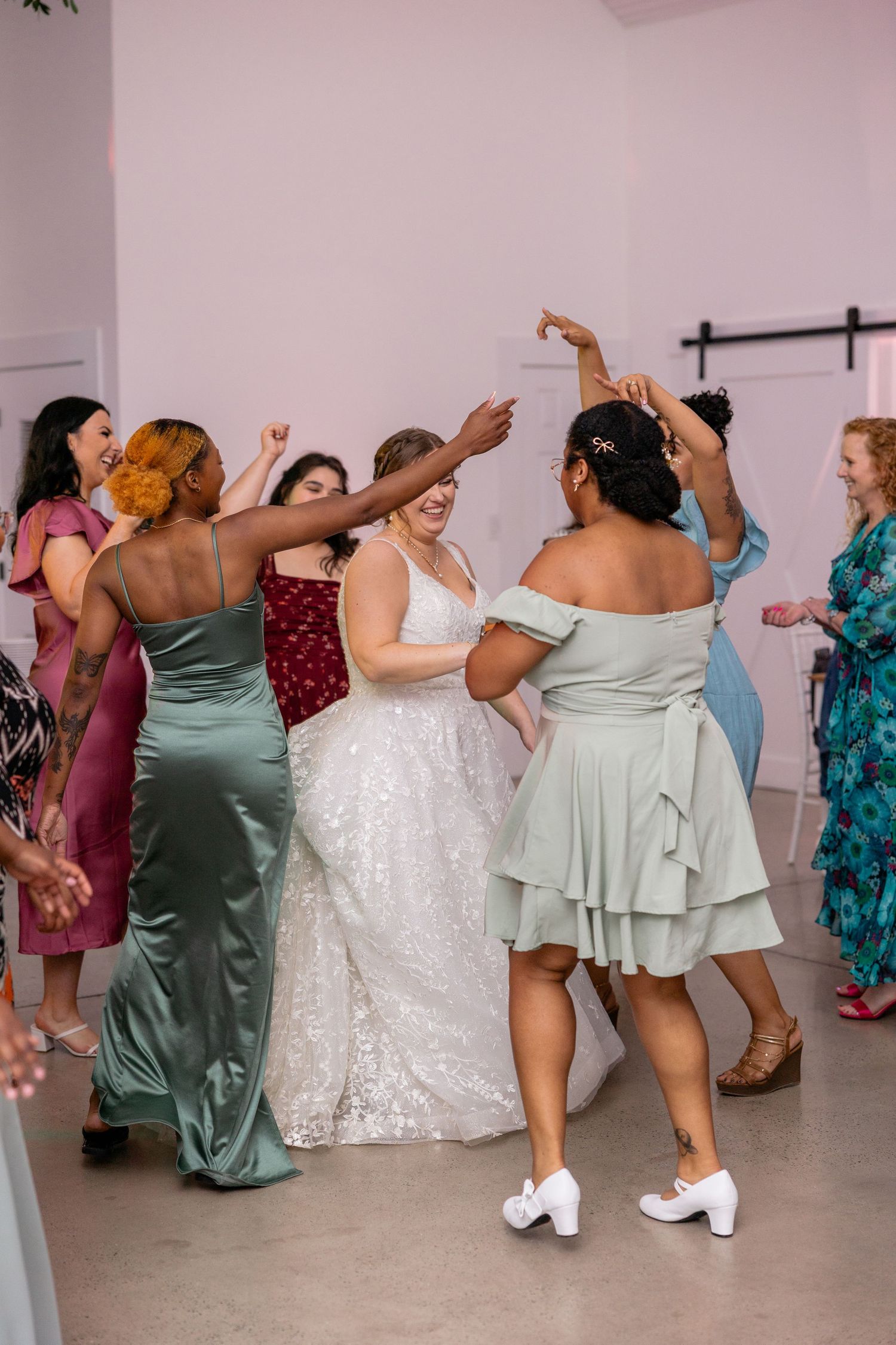 Joyful wedding guests dancing together in sage green and floral dresses at the reception.