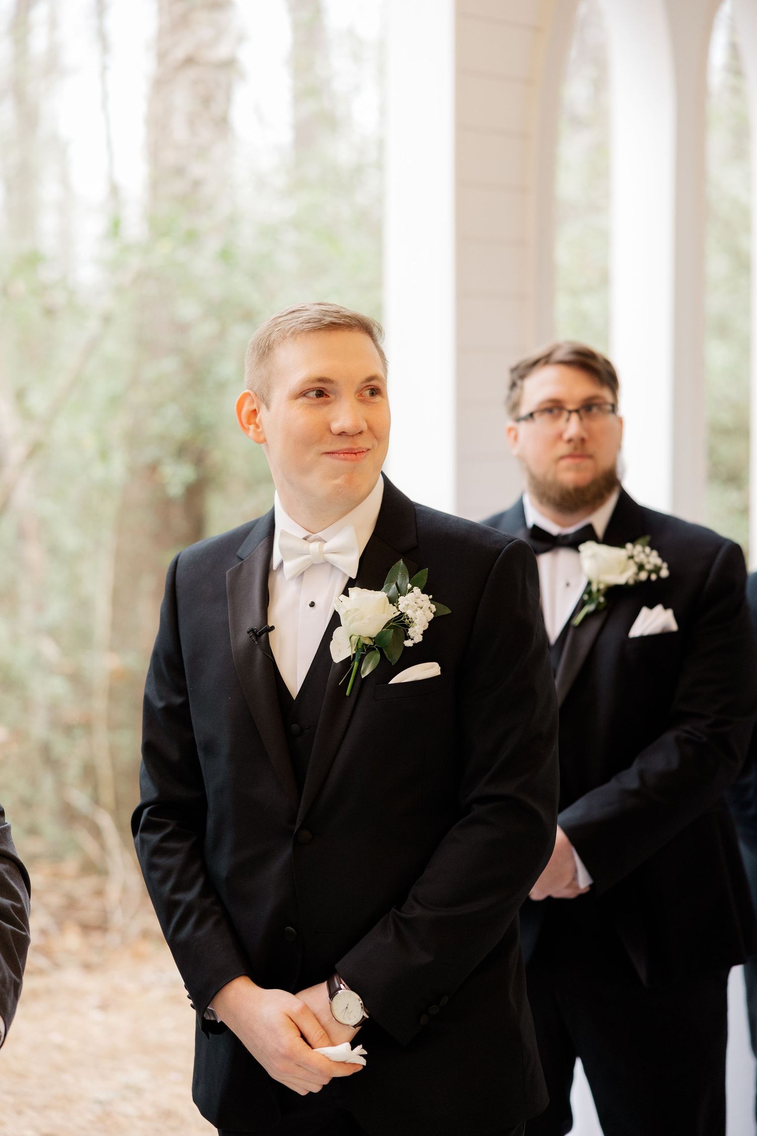 Formal wedding ceremony participants in black tuxedos at chapel altar.