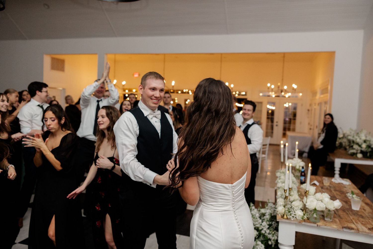 Energetic wedding reception dance floor scene with guests celebrating under indoor lighting.